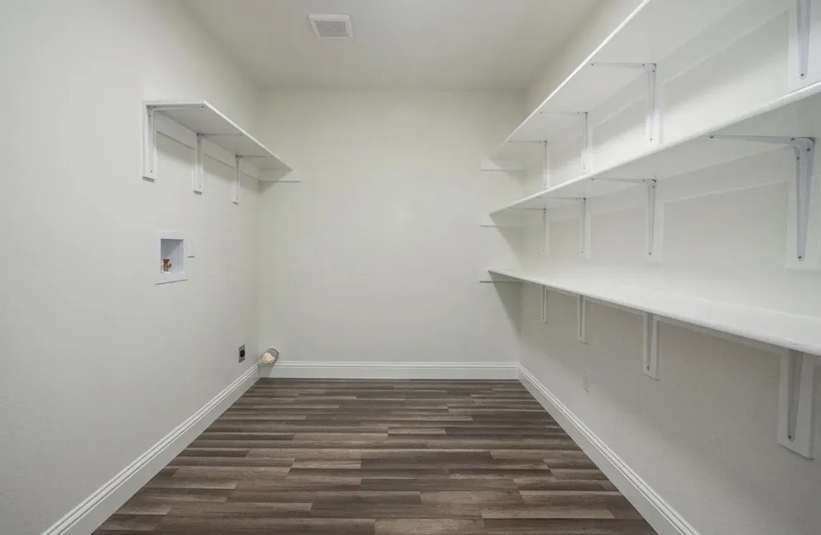 Dedicated laundry area featuring wood-finish flooring, white walls, and extensive built-in shelving for organization
