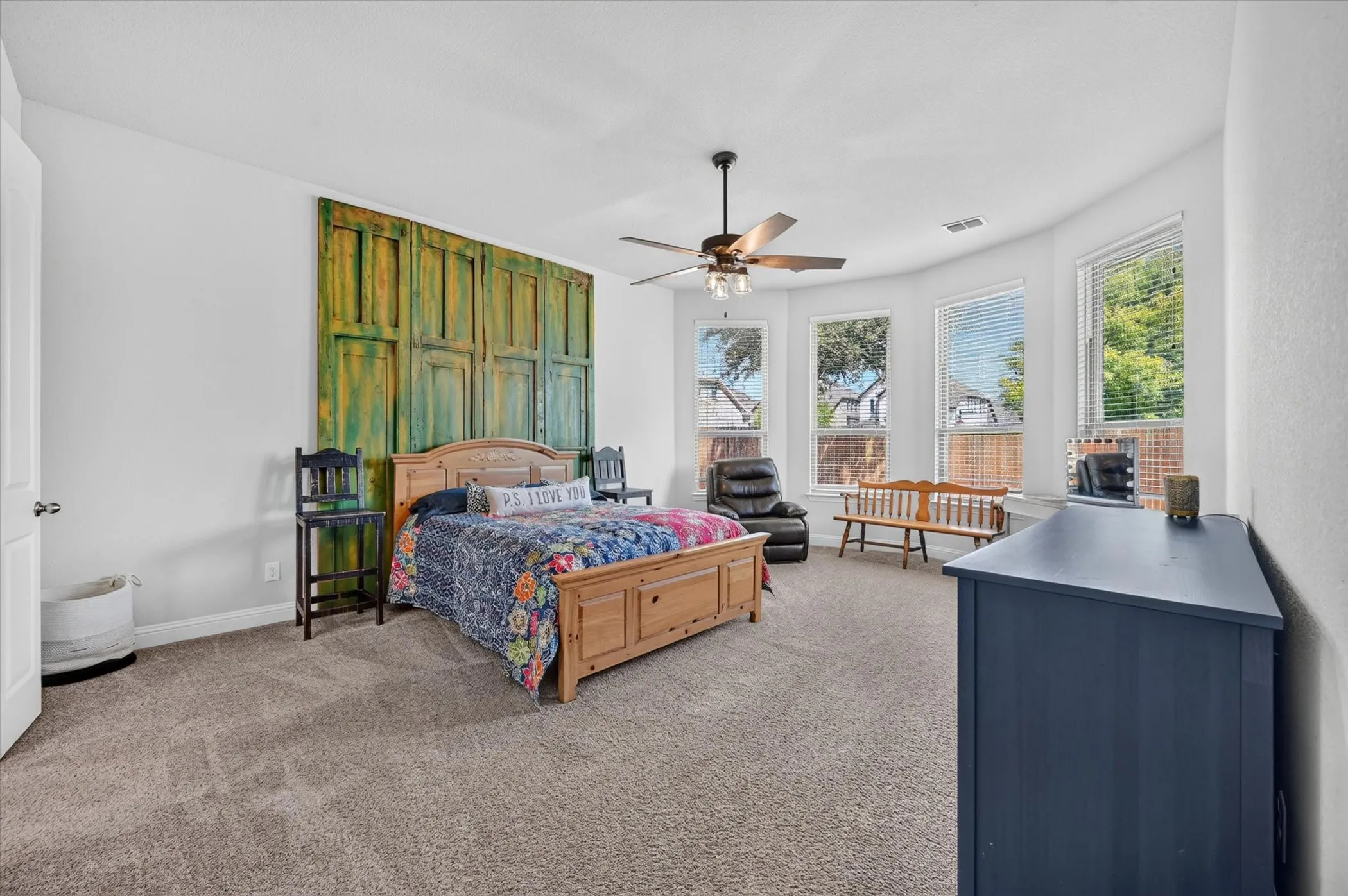 Spacious room featuring neutral carpet flooring, a ceiling fan with integrated lighting, and multiple windows with blinds