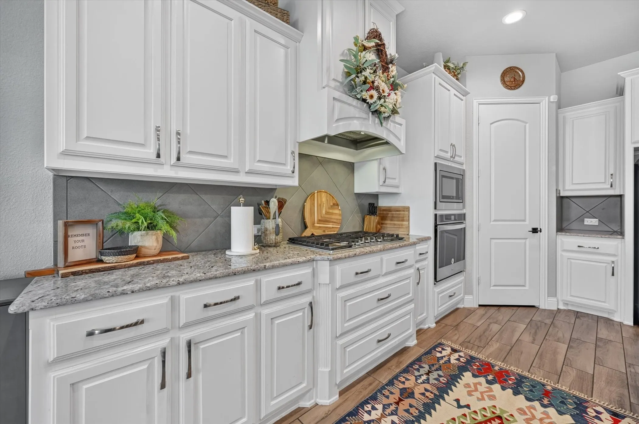 White cabinetry with polished hardware, stone countertops, a gas cooktop, and built-in double ovens