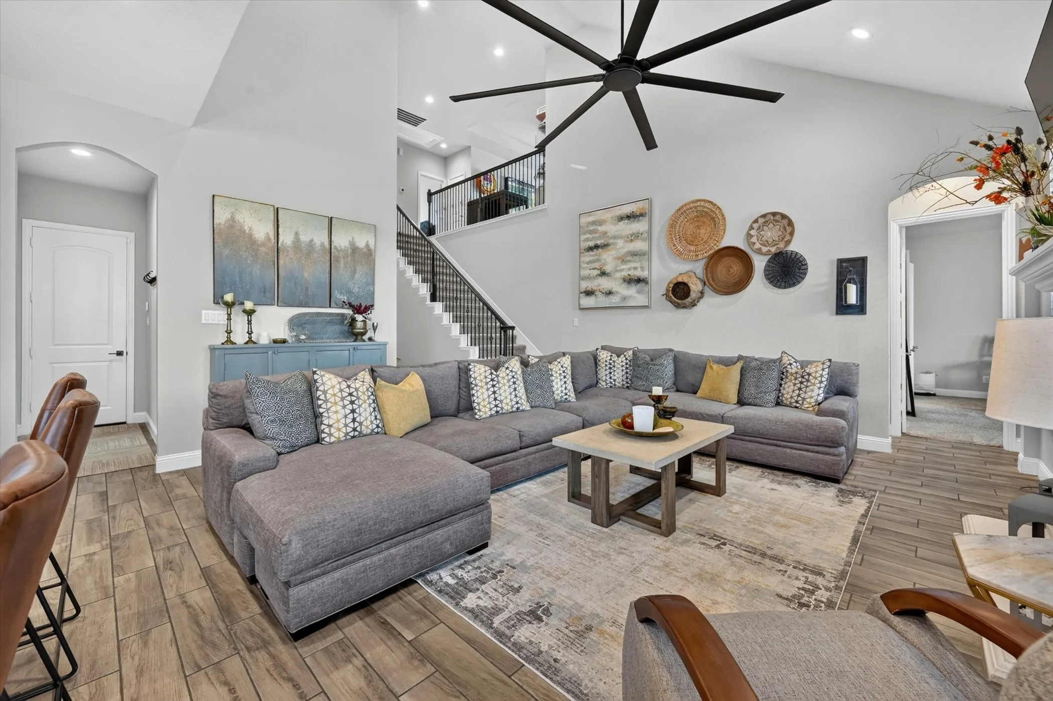 Spacious living area featuring vaulted ceilings, wood-finish flooring, a contemporary ceiling fan, and a staircase with an open iron railing