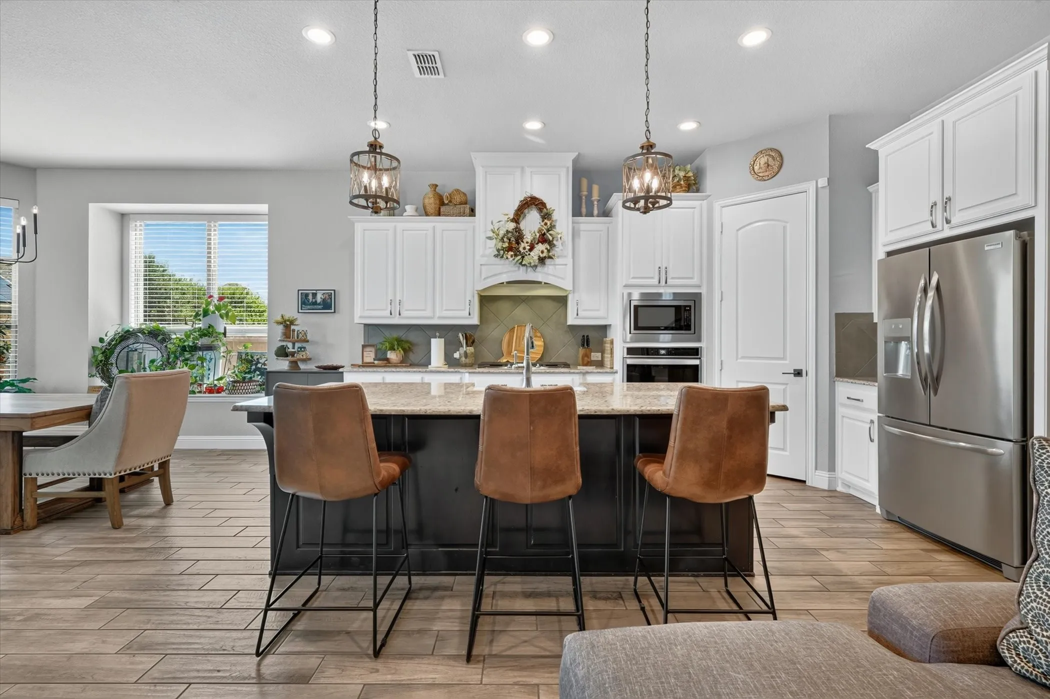 Open-concept kitchen featuring an island with a light-toned countertop, white cabinetry, integrated stainless steel appliances, and wood-finish flooring