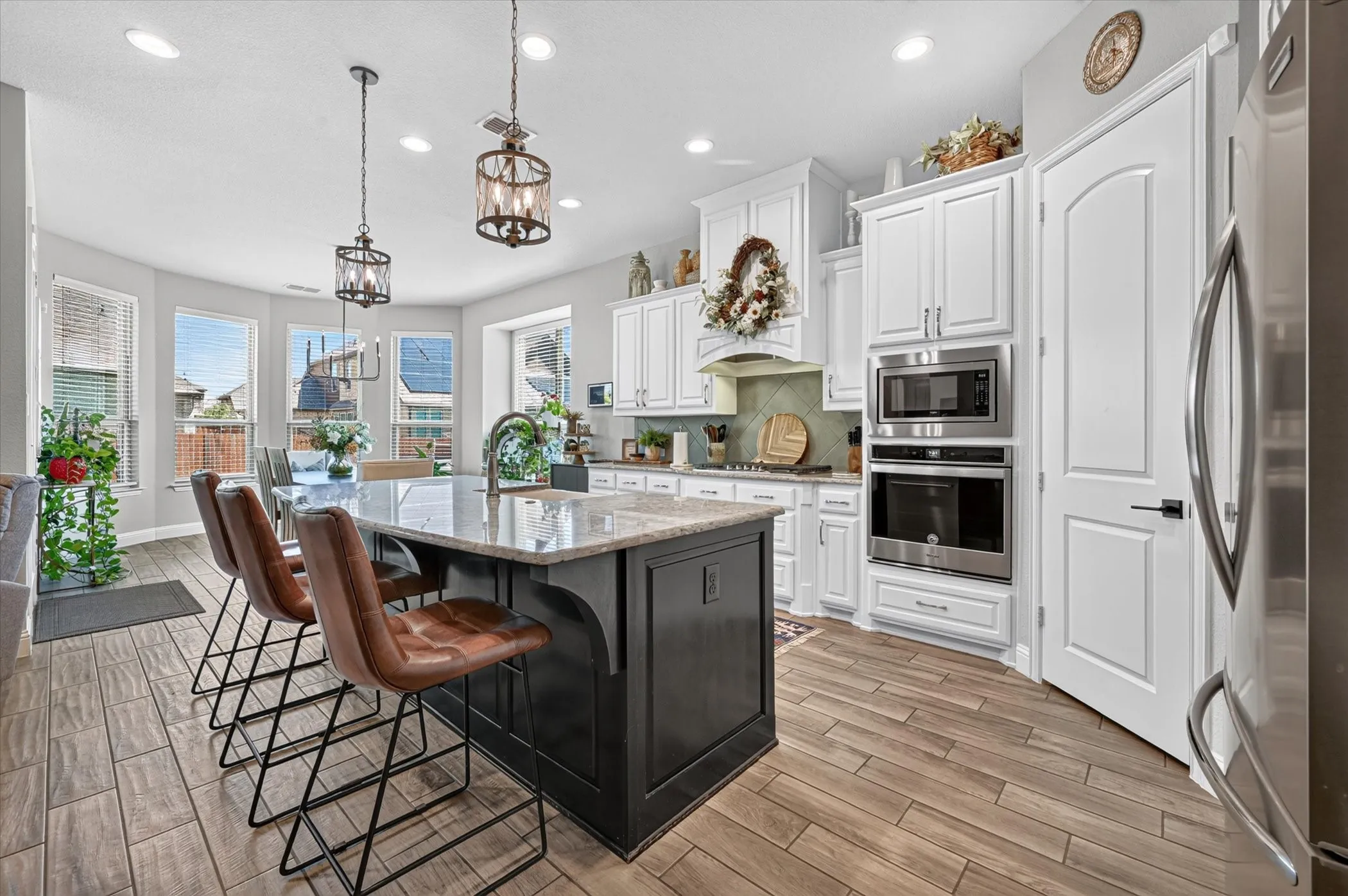 Expansive kitchen featuring a large central island with a stone countertop, wood-finish flooring, white cabinetry, integrated stainless steel appliances, and bay windows