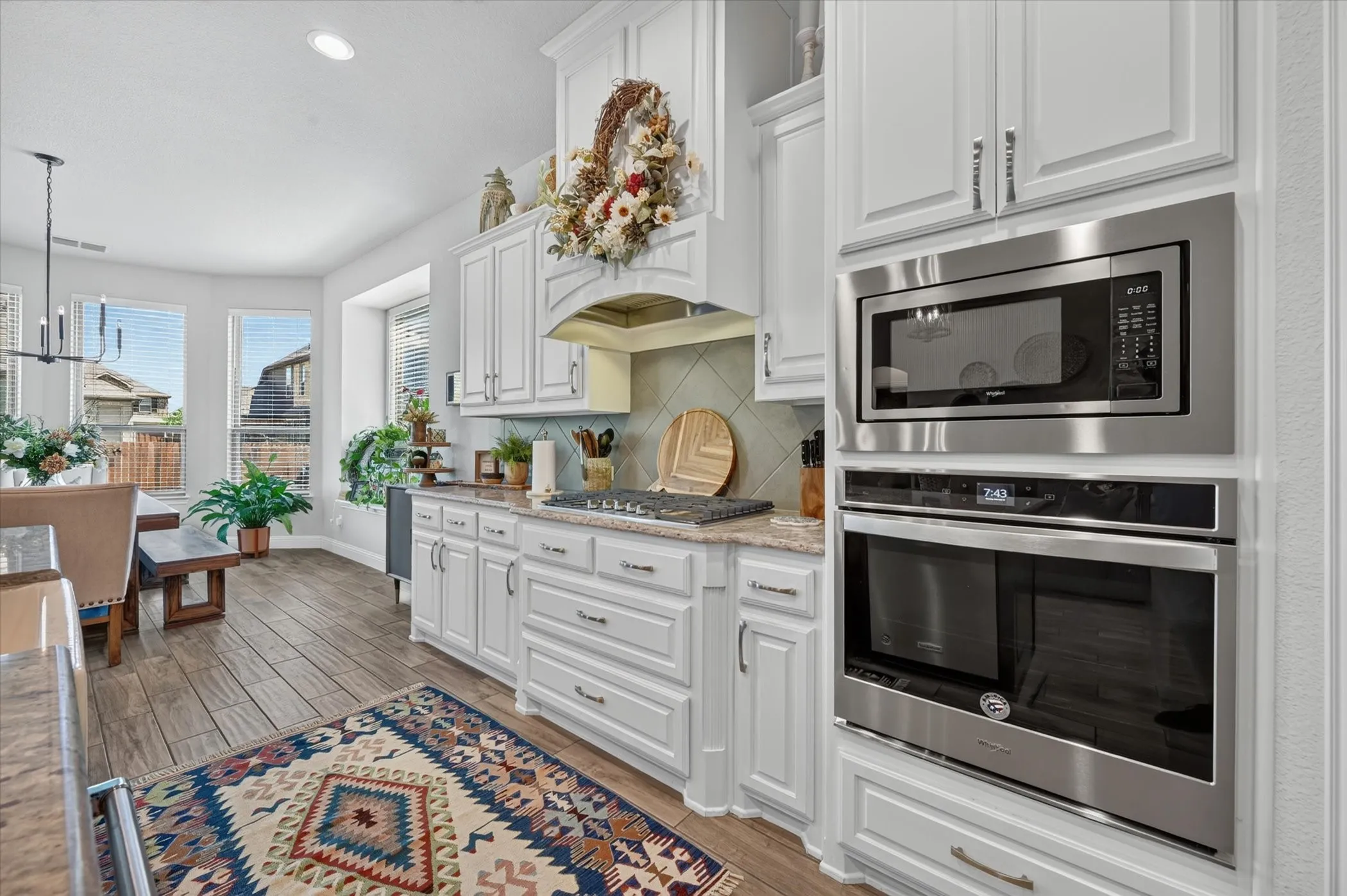 Kitchen featuring white cabinetry, built-in stainless steel appliances, wood-finish flooring, and a tiled backsplash