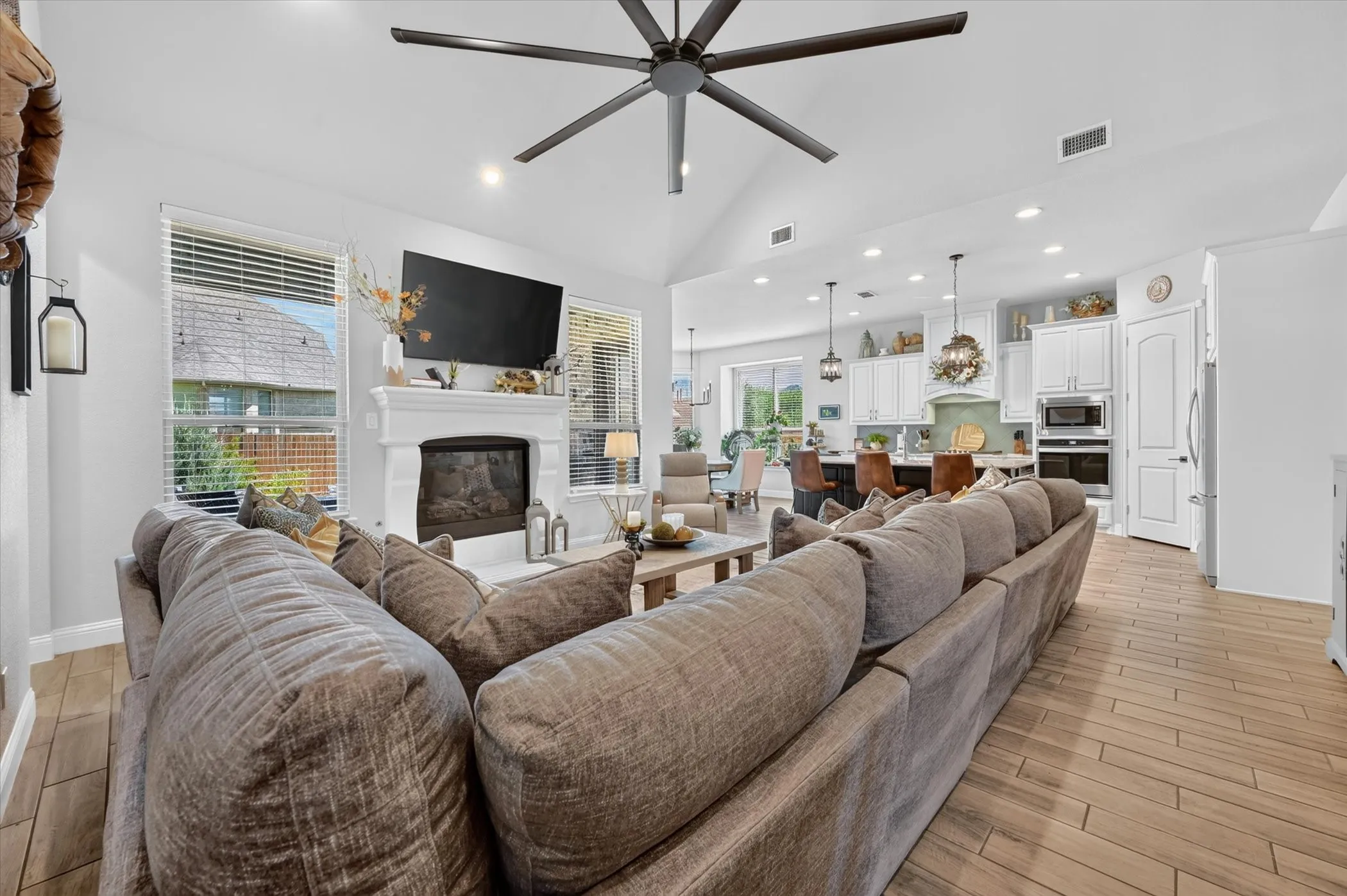 Vaulted ceiling living area featuring a fireplace with a white mantel, ceiling fan, and wood-finish flooring