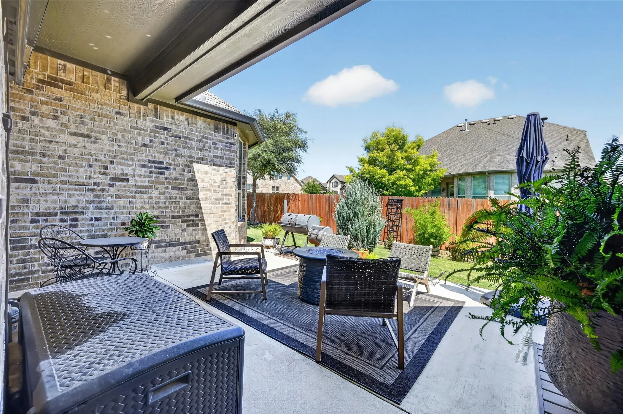 Covered outdoor patio with a concrete surface, gray brick exterior, and wood privacy fencing