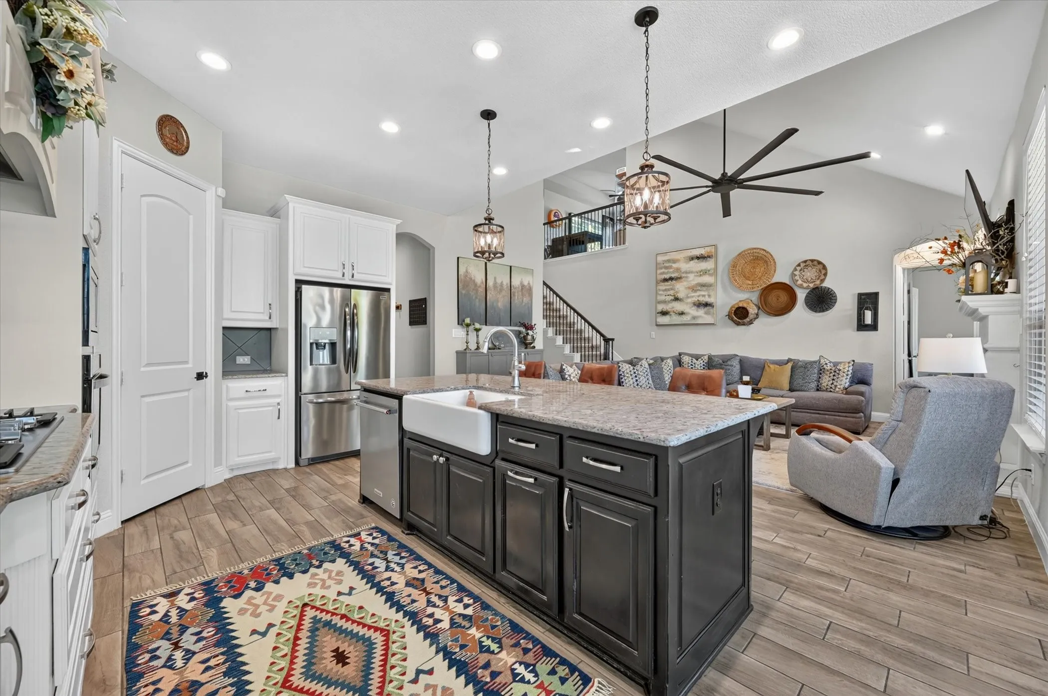 Open-concept kitchen featuring wood-finish flooring, a farmhouse sink, stainless steel appliances, and a large island with a stone-finish countertop