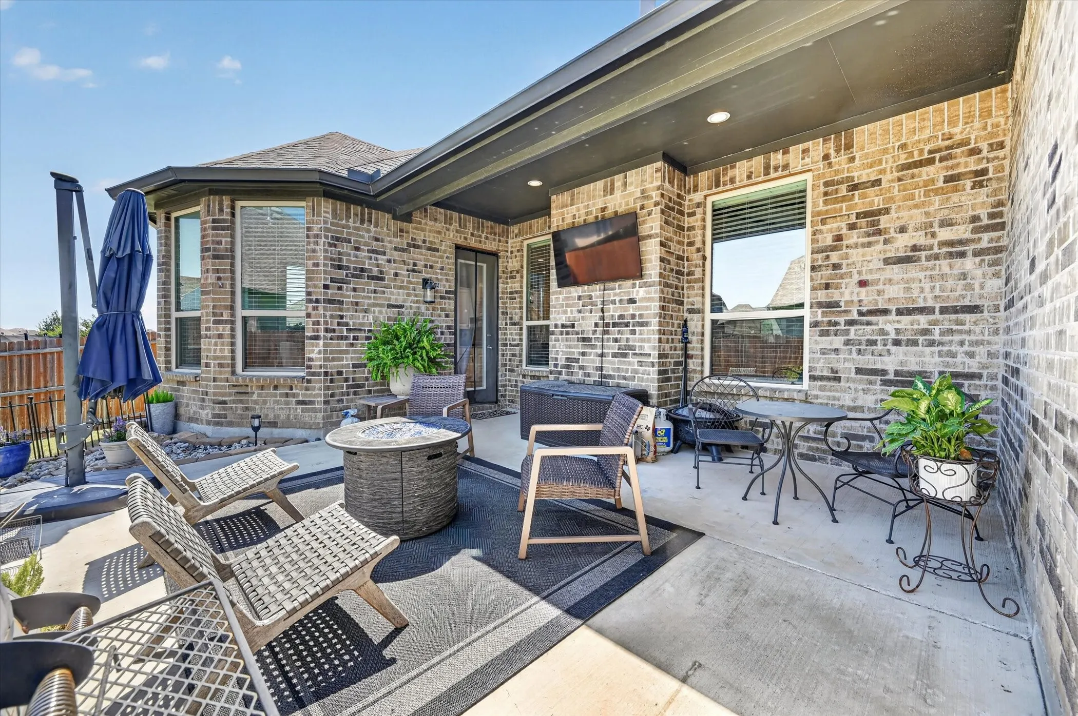 Expansive concrete patio area featuring a covered section with recessed lighting, brick exterior, bay window, and sliding glass door access