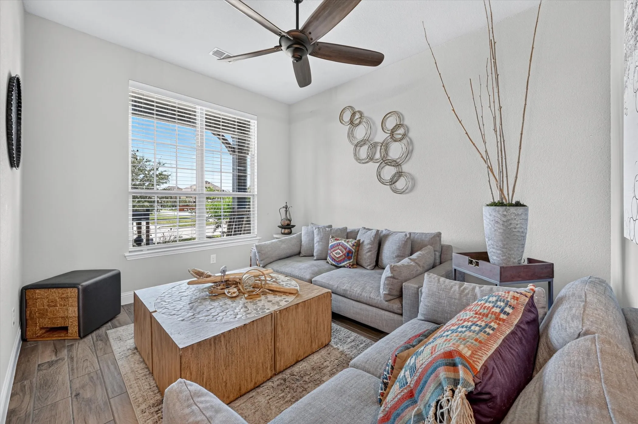Bright living space featuring wood-finish flooring, a ceiling fan, and a large window with white blinds