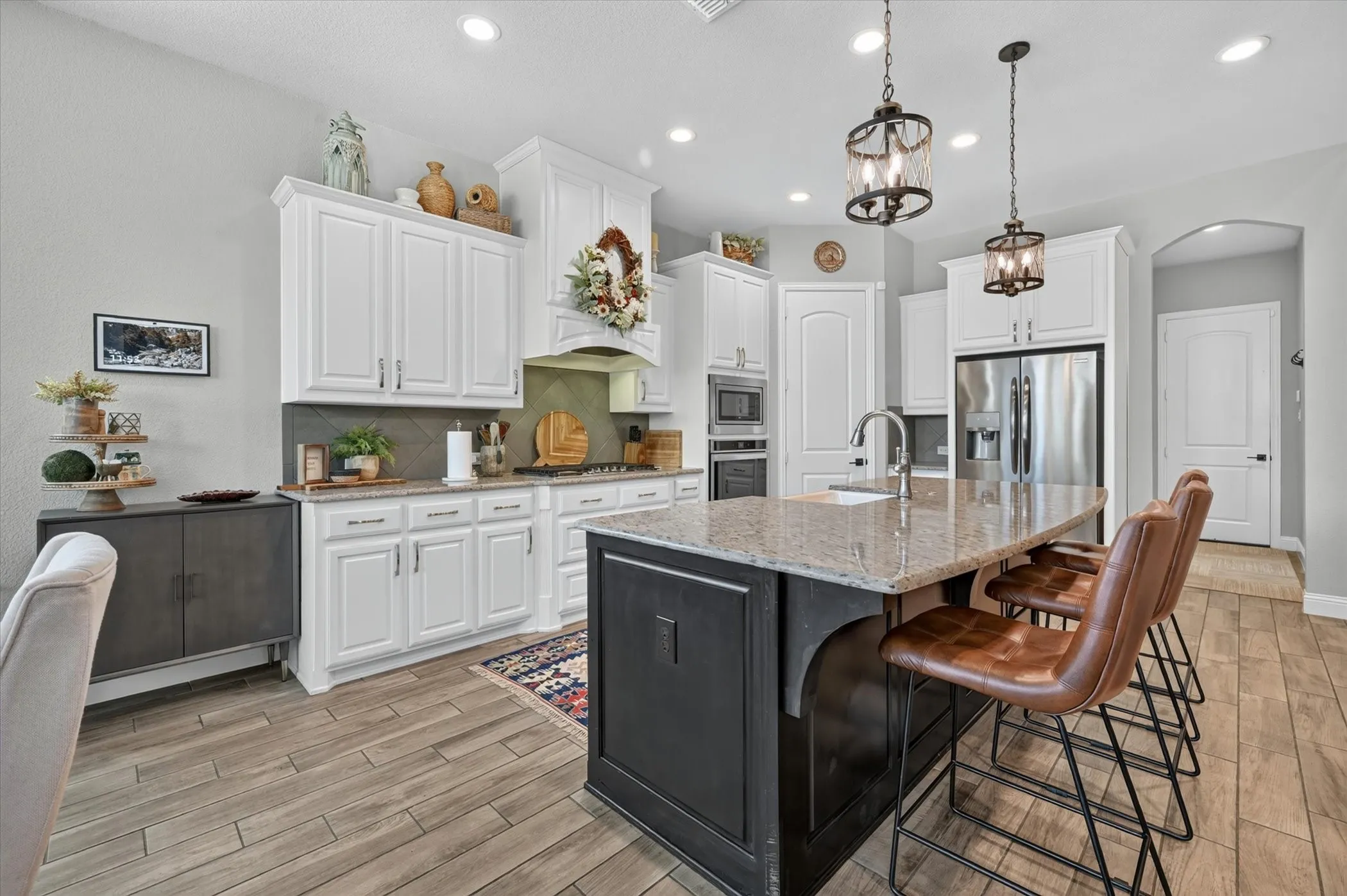 Kitchen featuring a dark-toned island with a light granite countertop, white cabinetry, wood-finish flooring, and recessed lighting