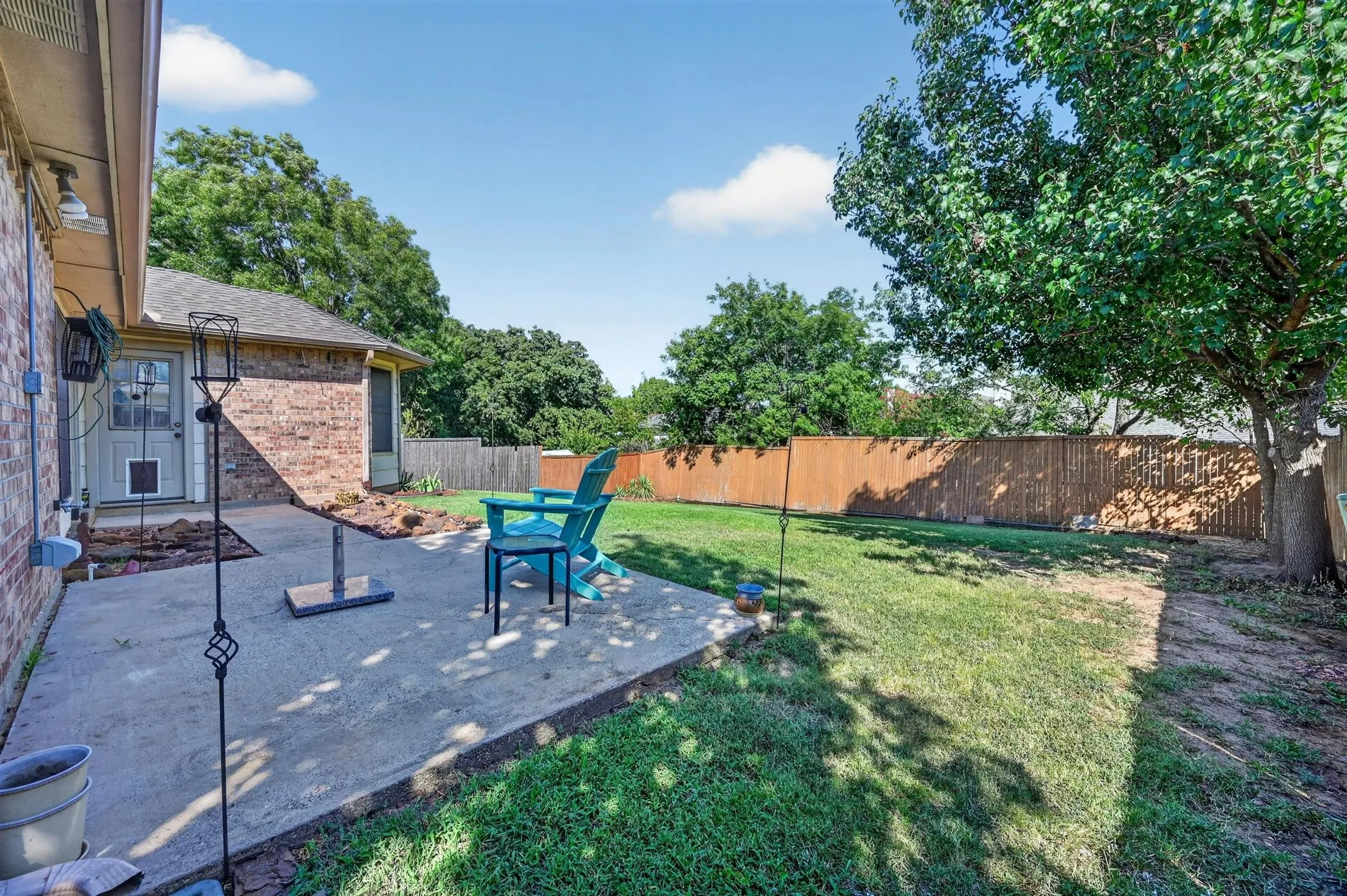 Expansive backyard featuring a concrete patio, a wooden privacy fence, and mature trees