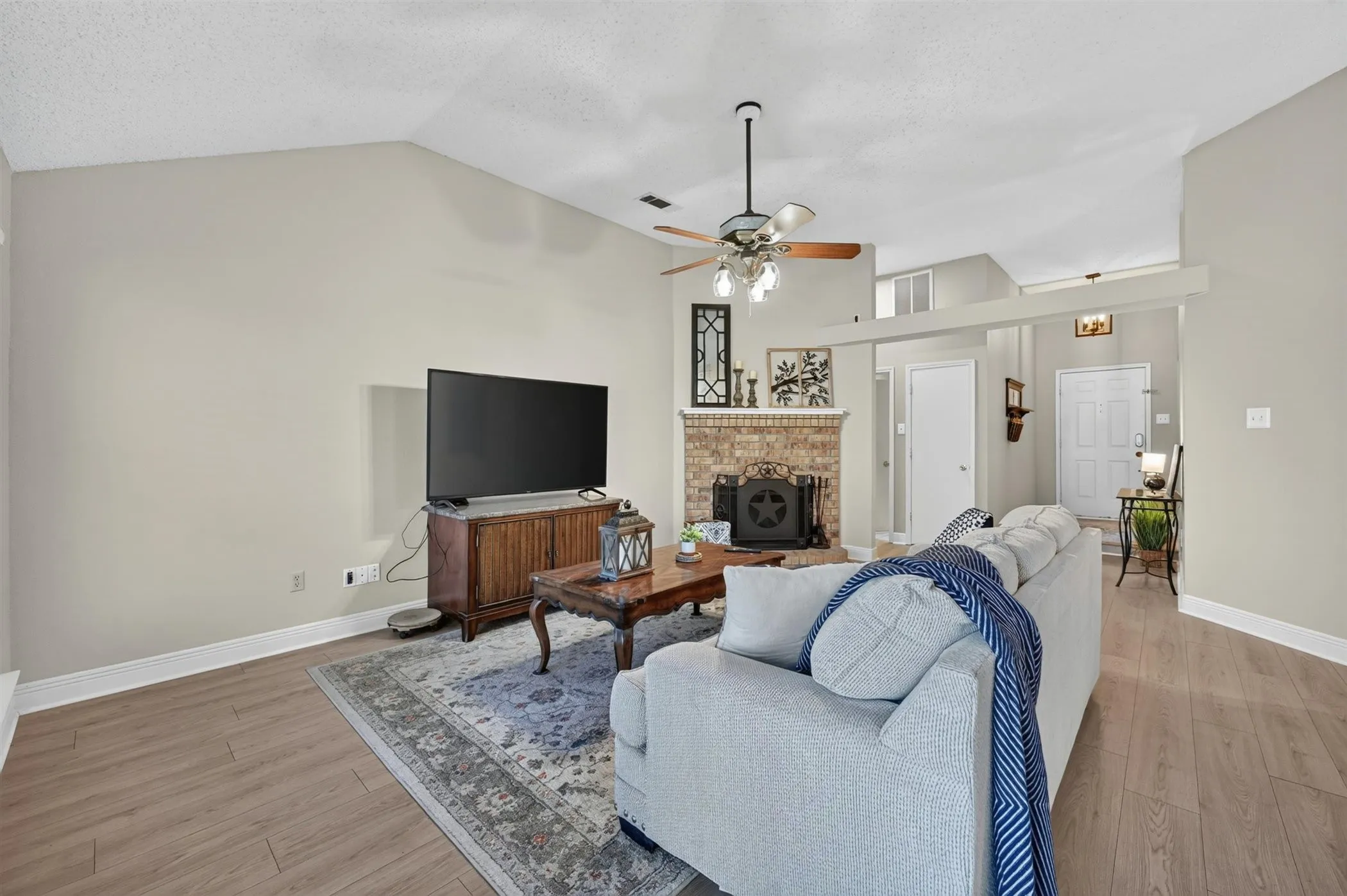 Spacious living area featuring wood-finish flooring, a vaulted ceiling, and a ceiling fan with integrated lighting