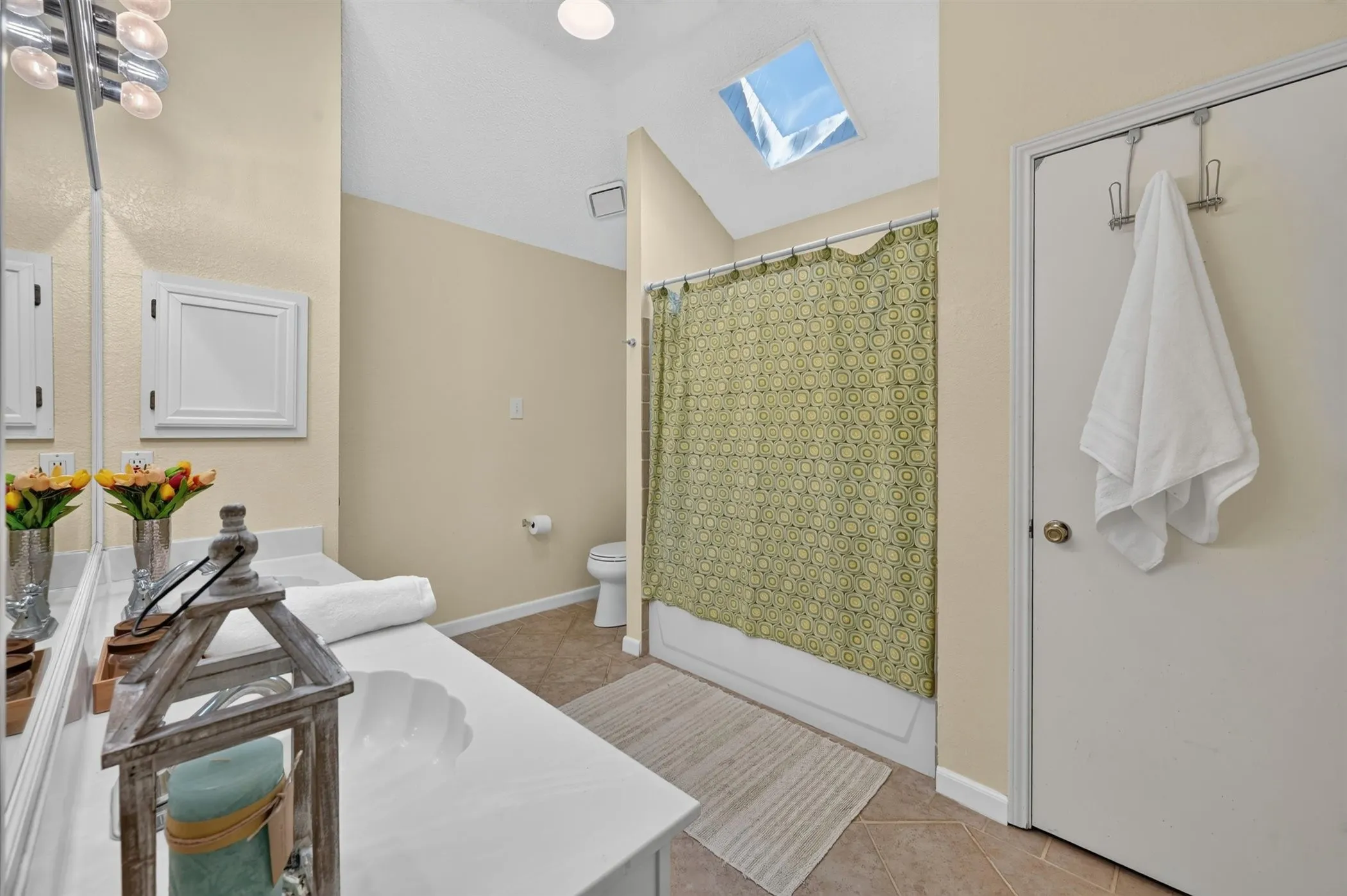 Bathroom featuring a vaulted ceiling with skylight, white vanity with integrated sink, chrome vanity lighting, and tile flooring