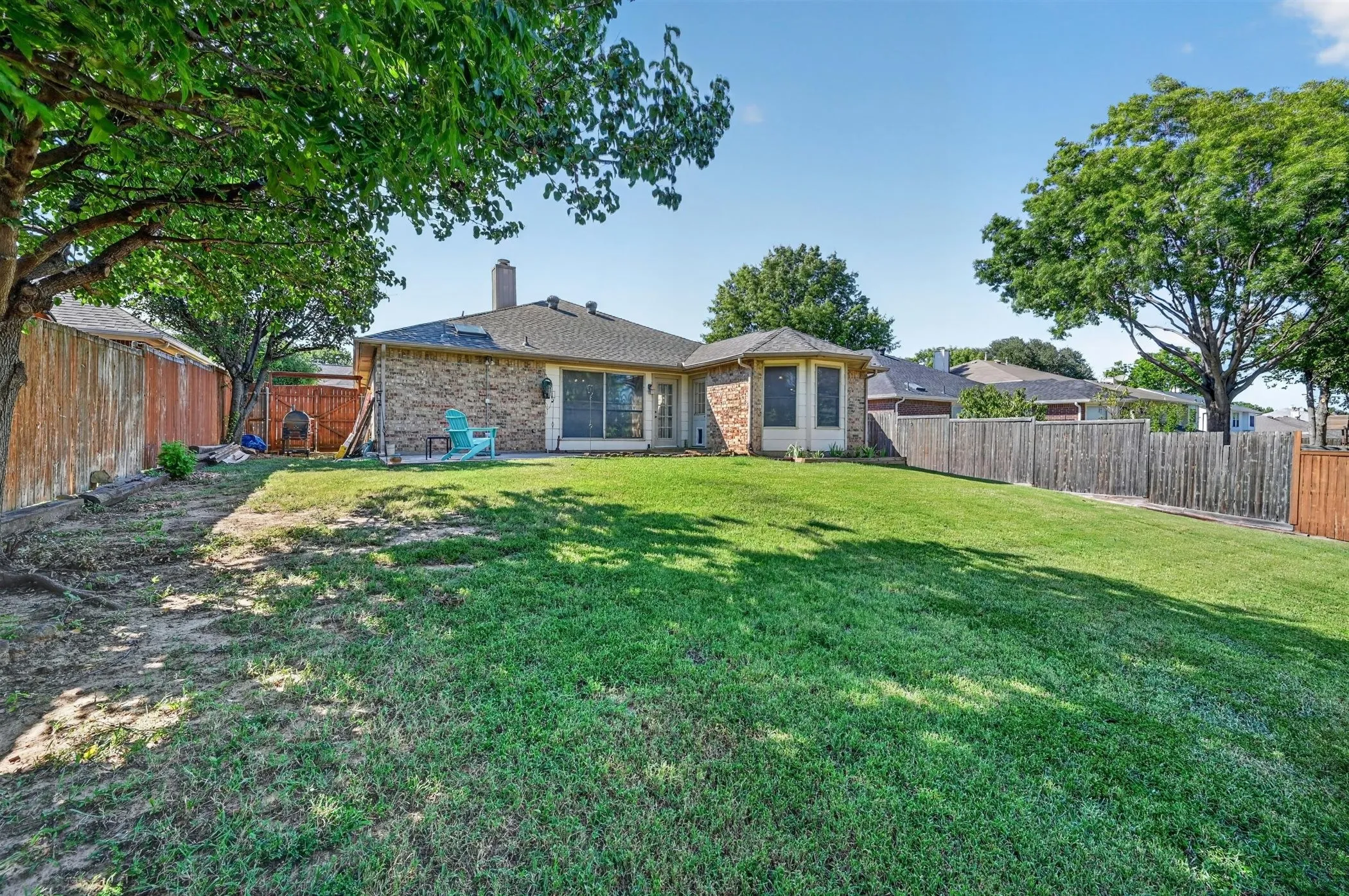 Expansive backyard featuring a large green lawn, mature trees, a brick patio, and privacy fencing