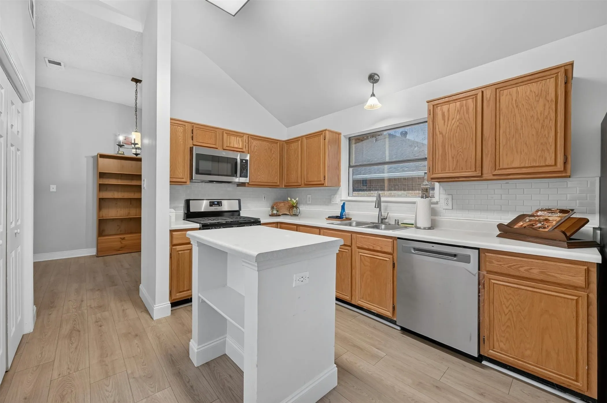 Kitchen featuring wood-finish cabinetry, stainless steel appliances, white subway tile backsplash, and light wood-finish flooring