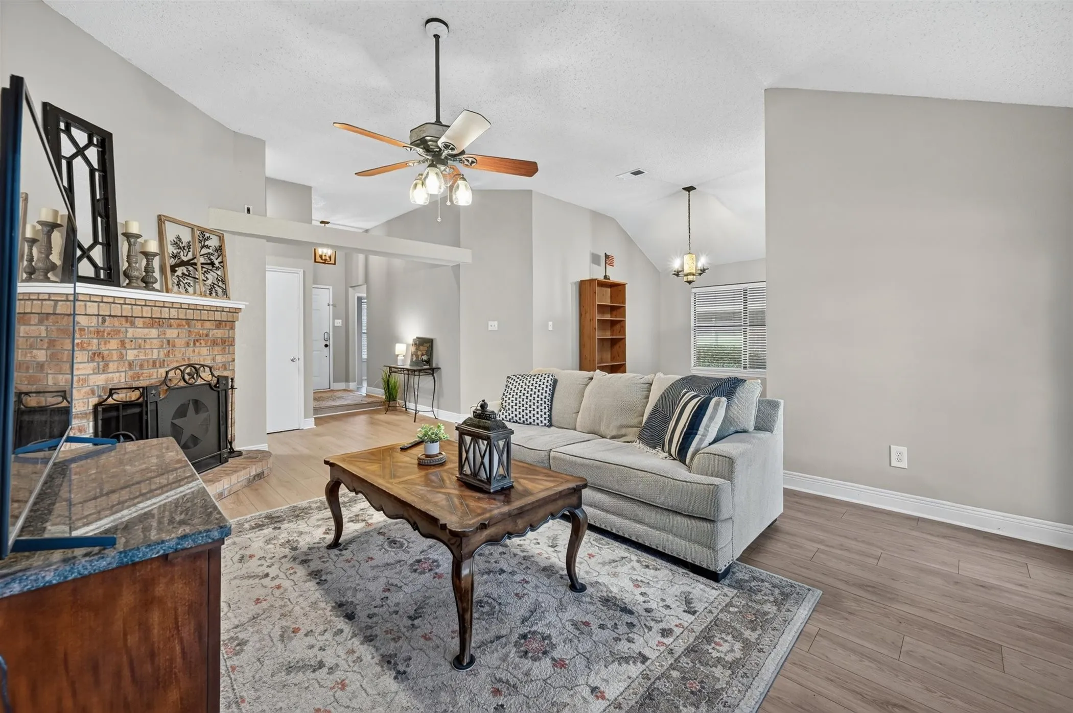 Spacious living area featuring a brick fireplace with a custom screen, vaulted ceilings, and wood-finish flooring