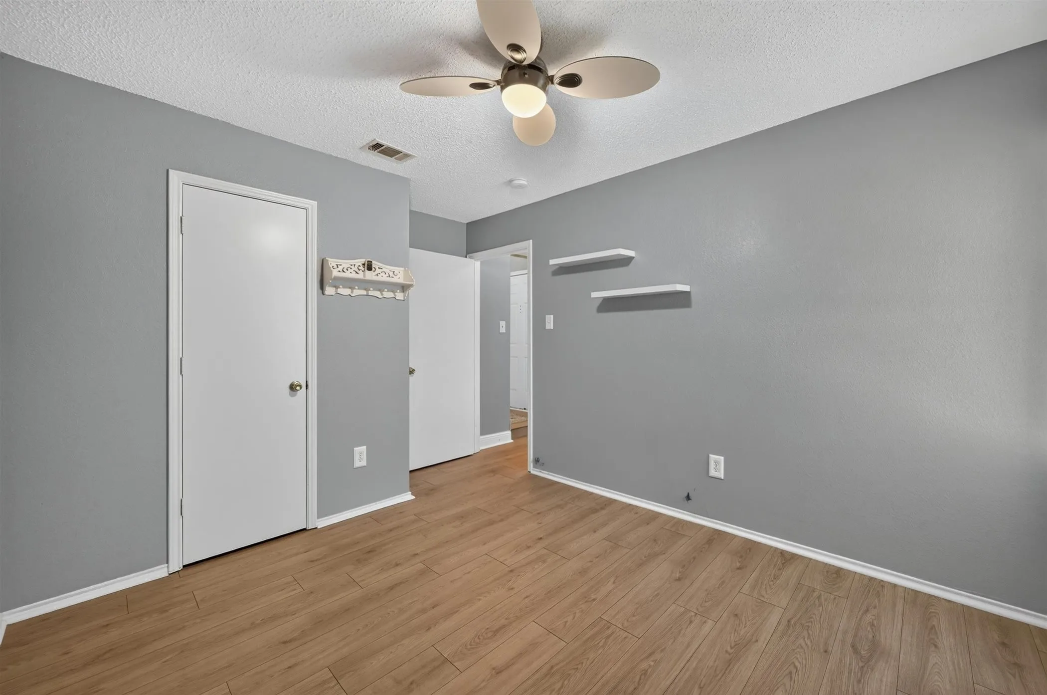 Room featuring wood-finish flooring, light gray walls, white trim, and a ceiling fan with integrated lighting
