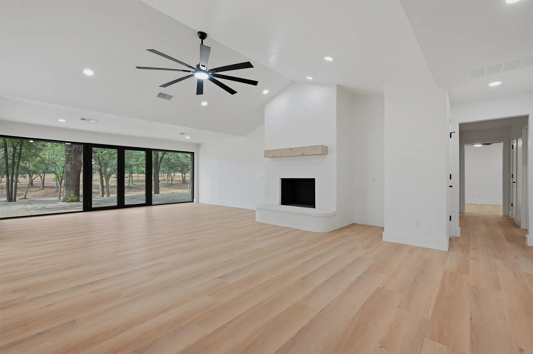 Spacious room featuring light wood-finish flooring, a vaulted ceiling with a large ceiling fan, and recessed lighting