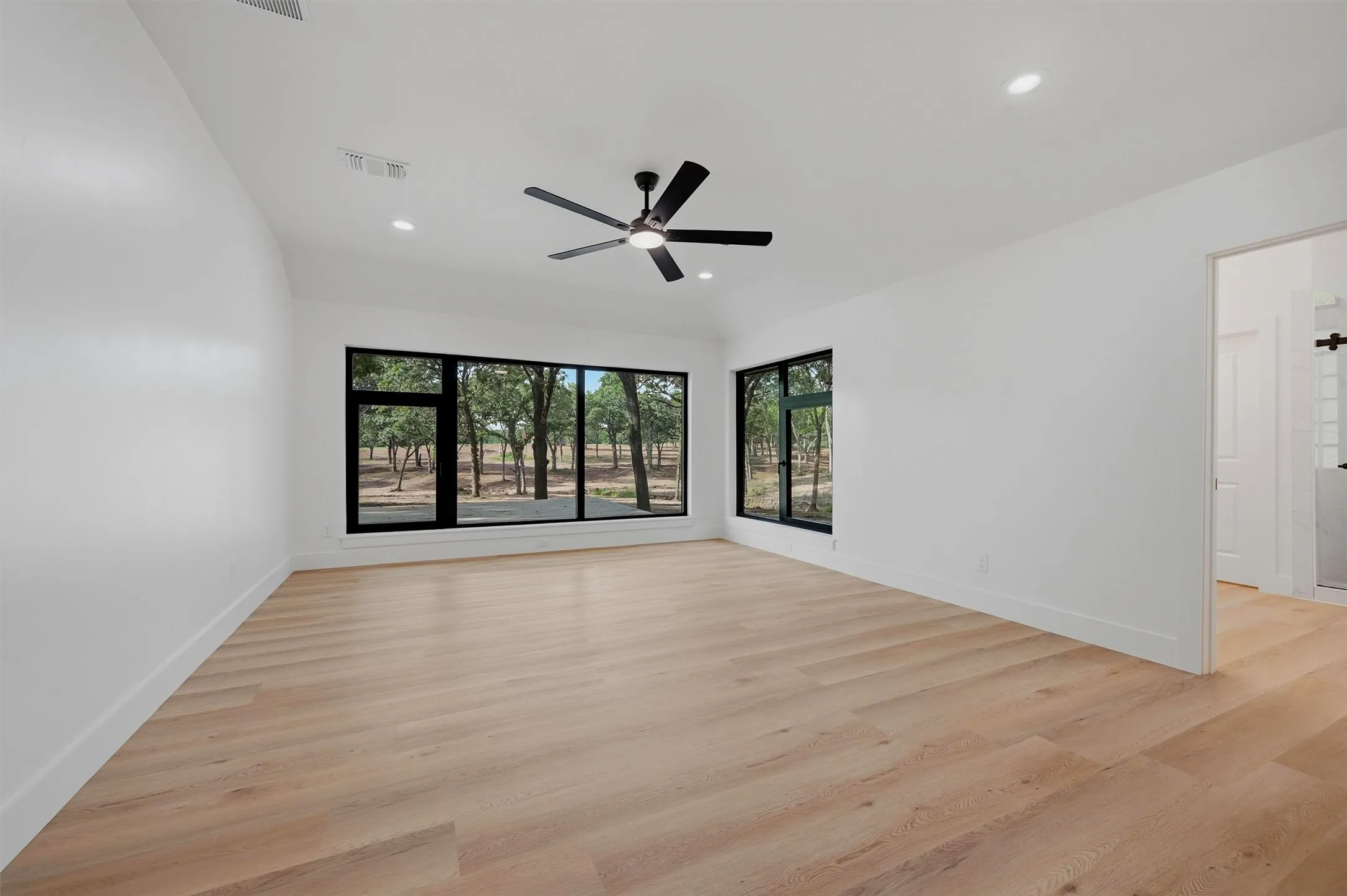 Spacious room featuring multiple large windows with black frames, wood-finish flooring, a contemporary ceiling fan, and recessed lighting