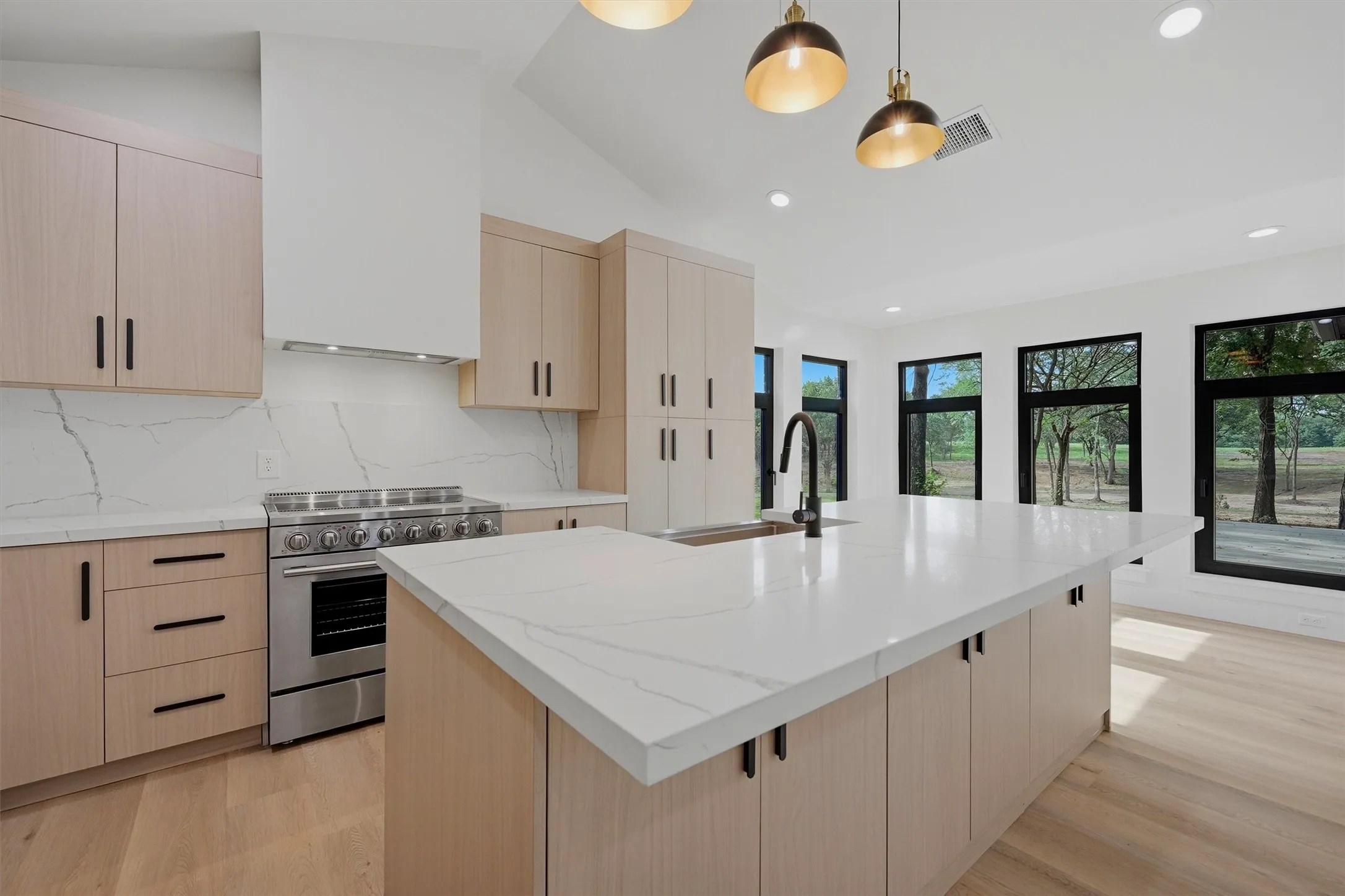 Spacious kitchen featuring light wood-finish cabinetry, a large center island with a white countertop, a black gooseneck faucet, and a stainless steel professional range