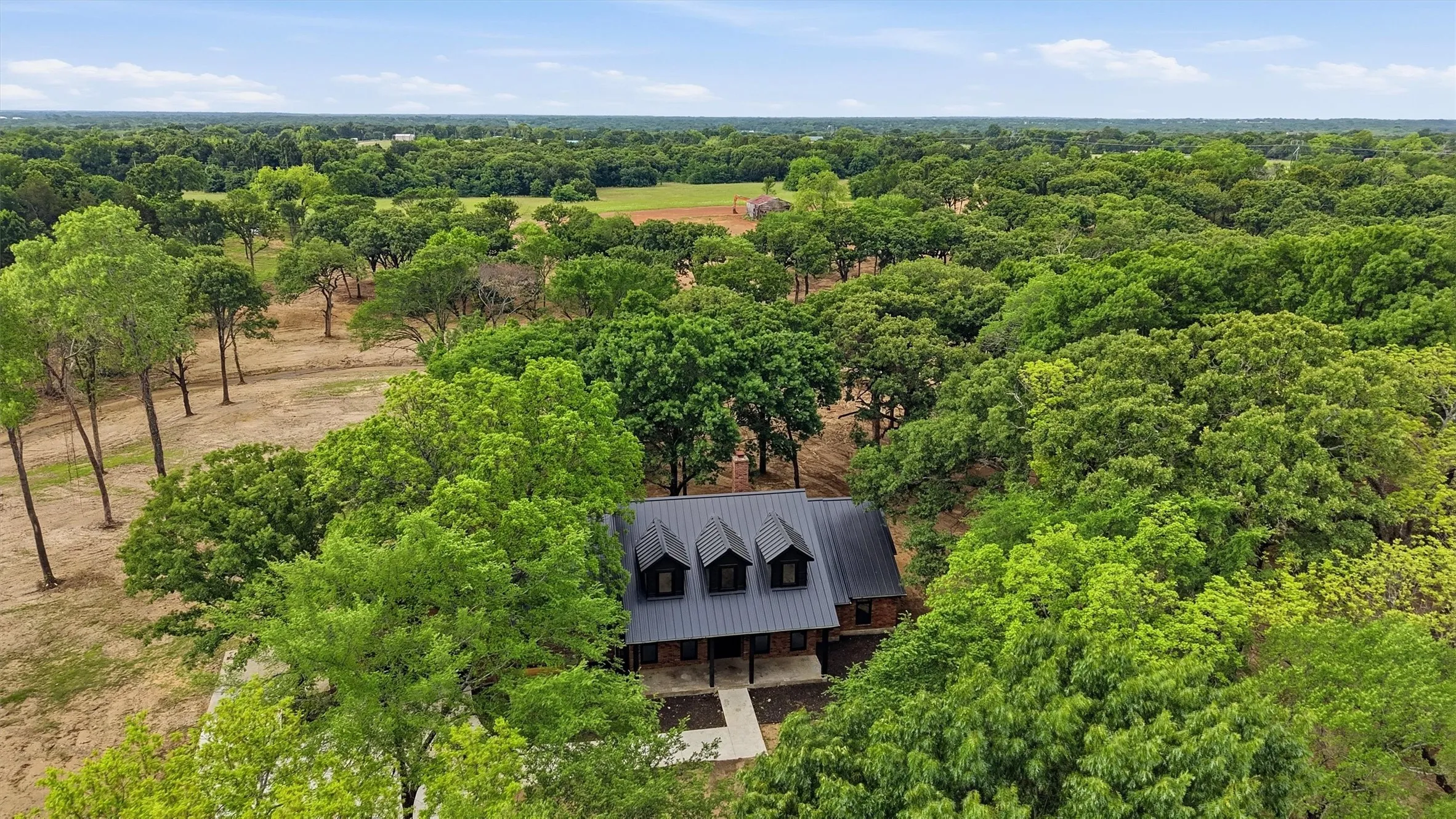 Expansive property featuring a residence with a dark metal roof, multiple dormer windows, and a brick exterior