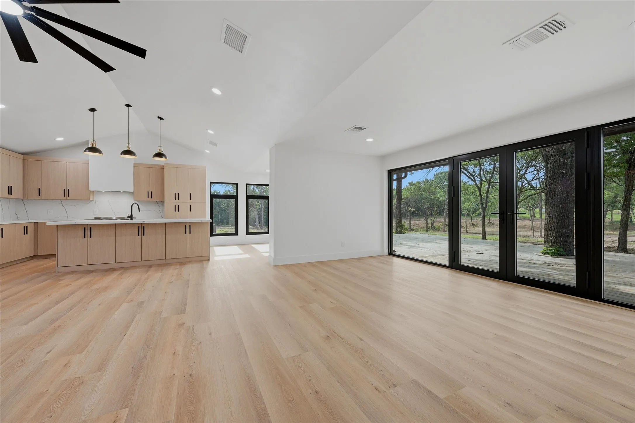 Open-concept living space featuring light wood-finish flooring, a vaulted ceiling with recessed lighting, and a contemporary ceiling fan