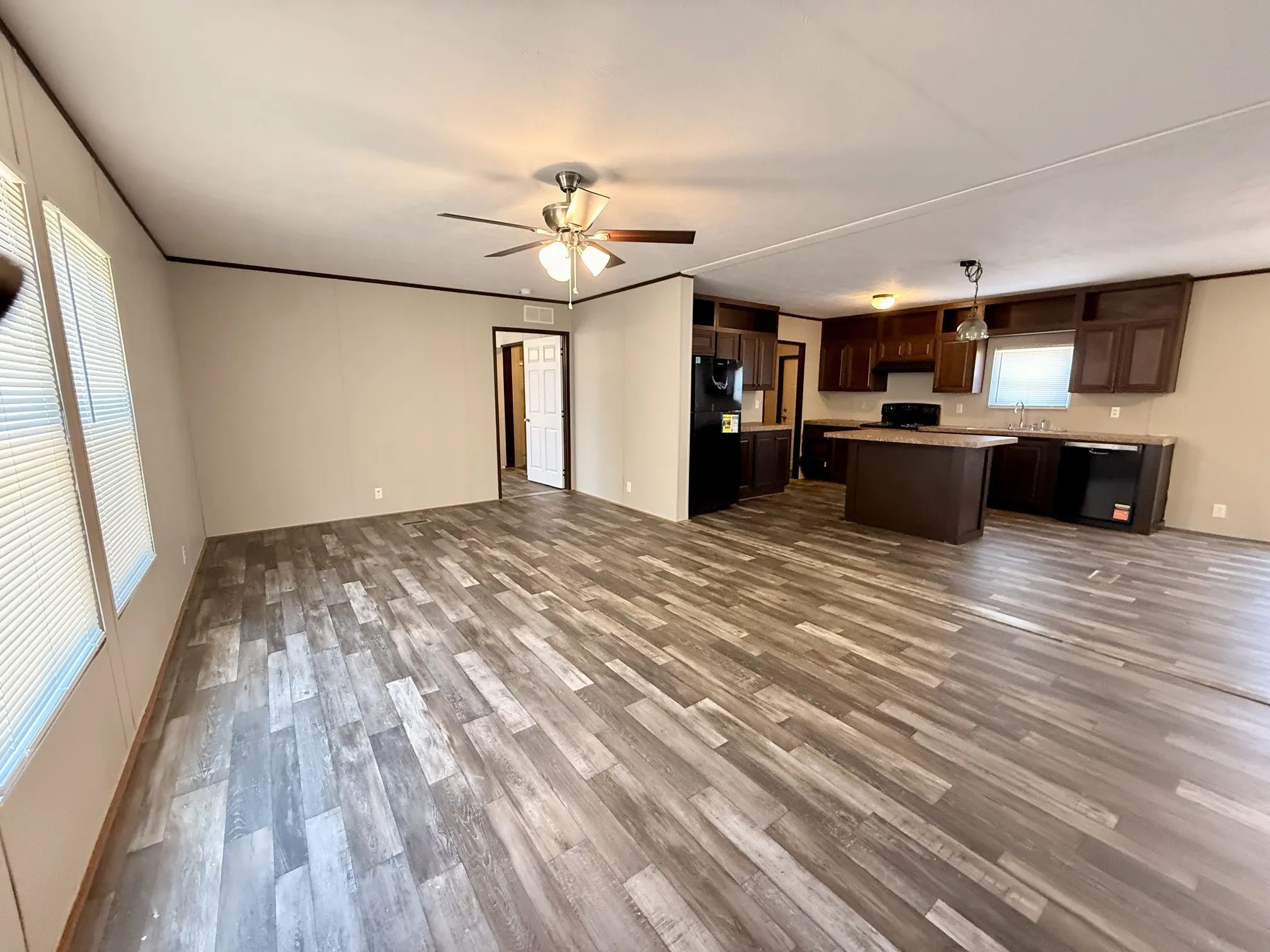 Open-concept living area featuring wood-finish flooring, a ceiling fan, and multiple windows with blinds