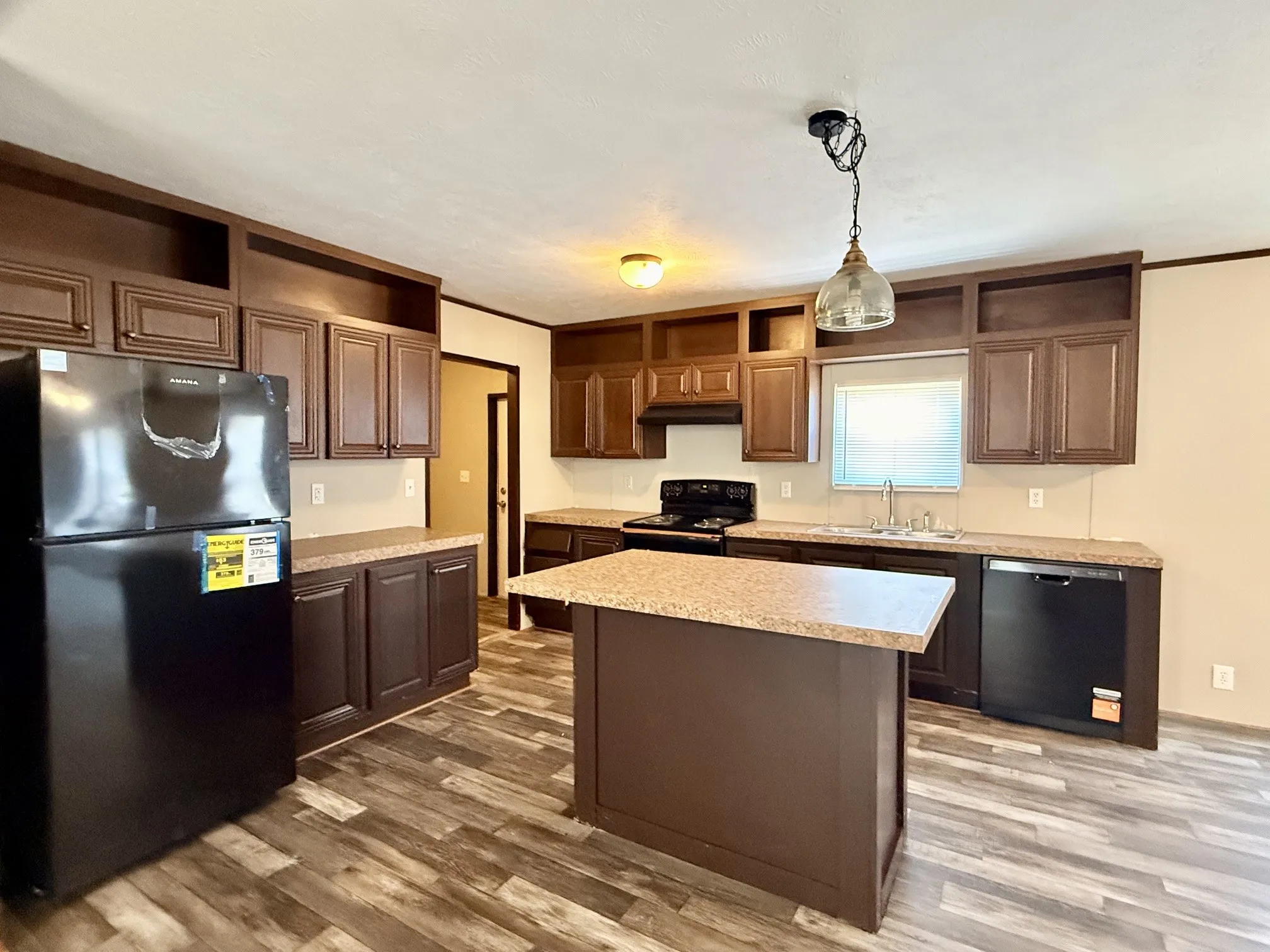 Kitchen featuring an eat-at island, dark wood-finish cabinetry, black appliances, and multi-toned wood-finish flooring