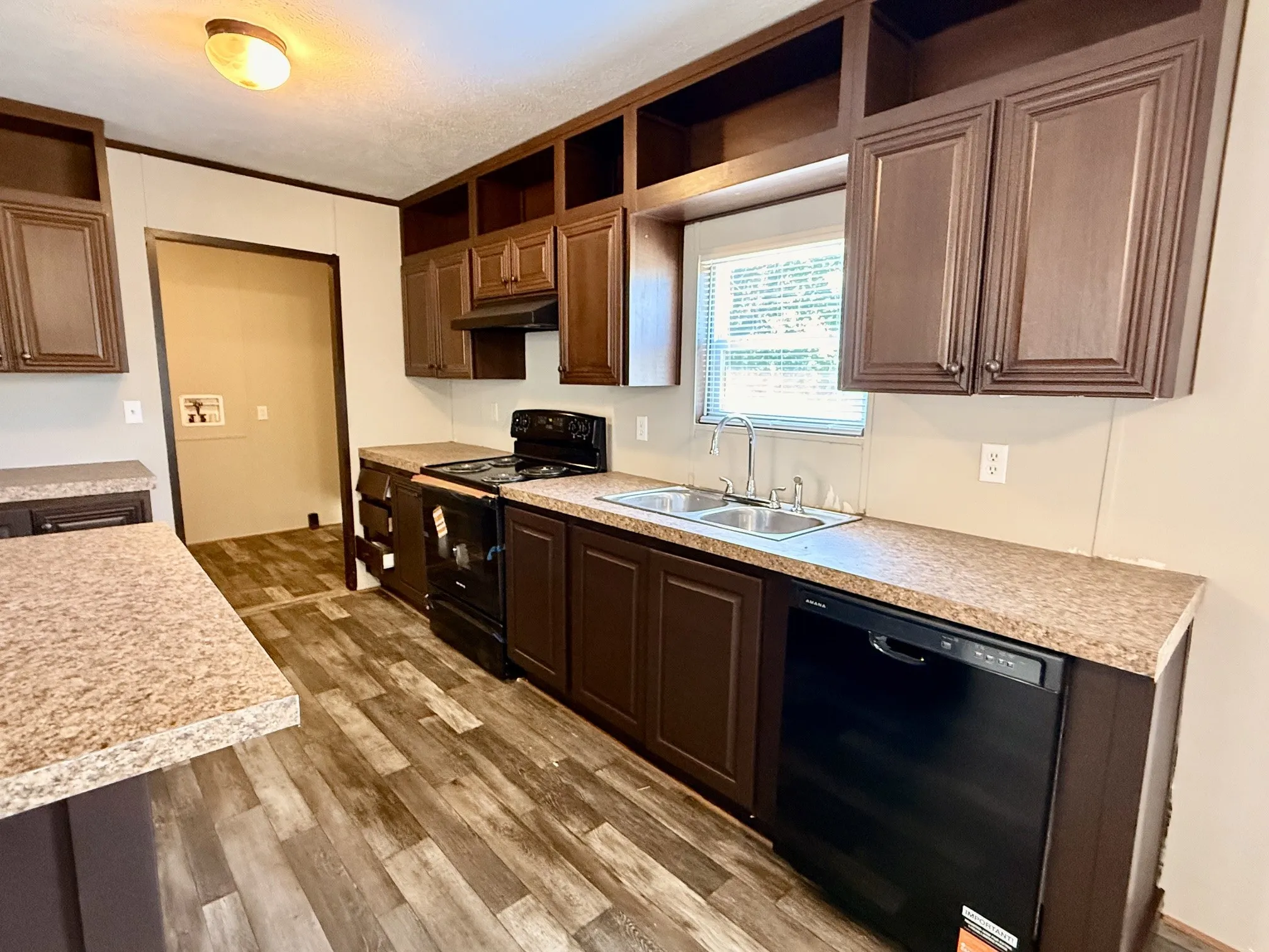 Kitchen featuring wood-finish flooring, dark wood cabinetry, speckled countertops, a double basin stainless steel sink, and a black appliance suite