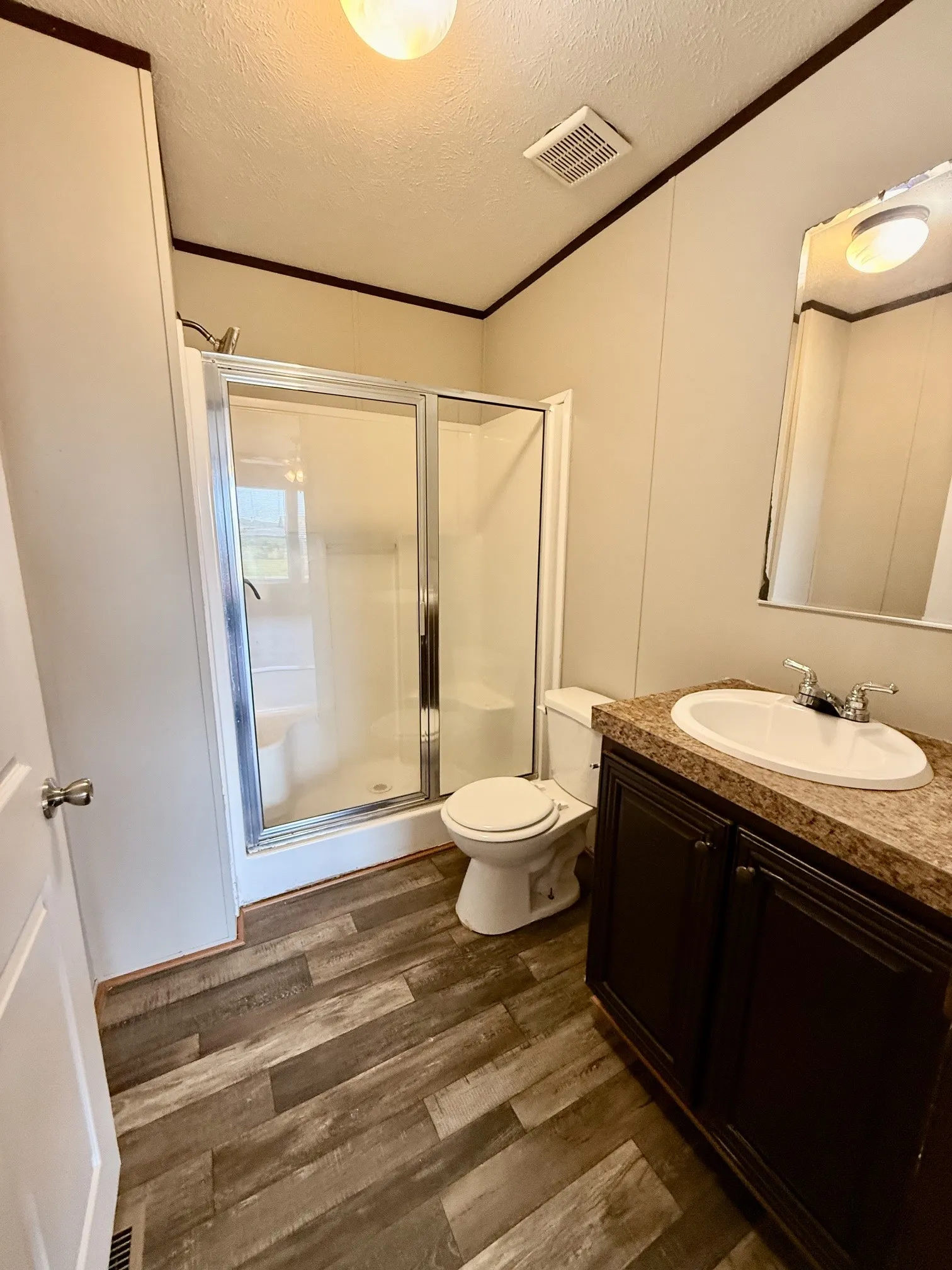 Bathroom featuring a shower with glass enclosure, single vanity with dark cabinetry, integrated sink, and wood-finish flooring