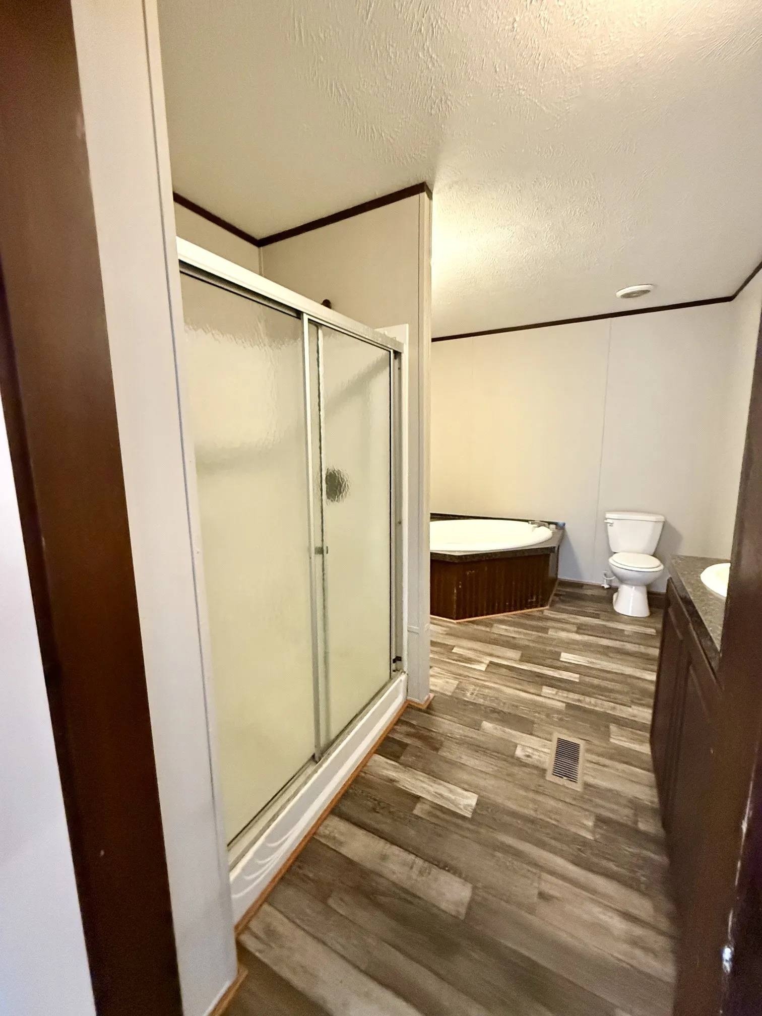Bathroom featuring a sliding glass door shower, a built-in corner soaking tub with wood-finish paneling, a toilet, and wood-finish flooring