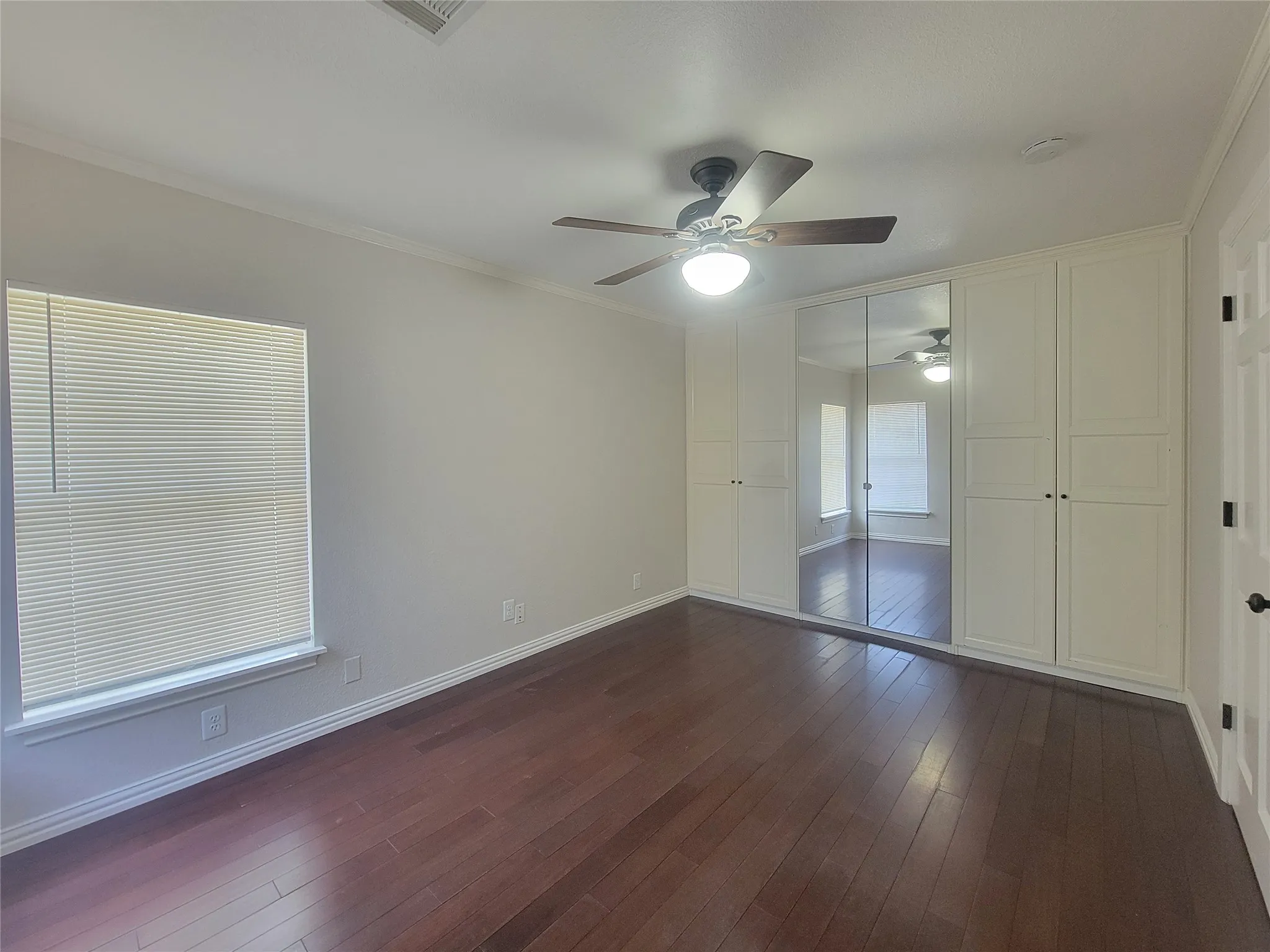 Spacious room featuring wood-finish flooring, a ceiling fan, and extensive built-in cabinetry with mirrored doors