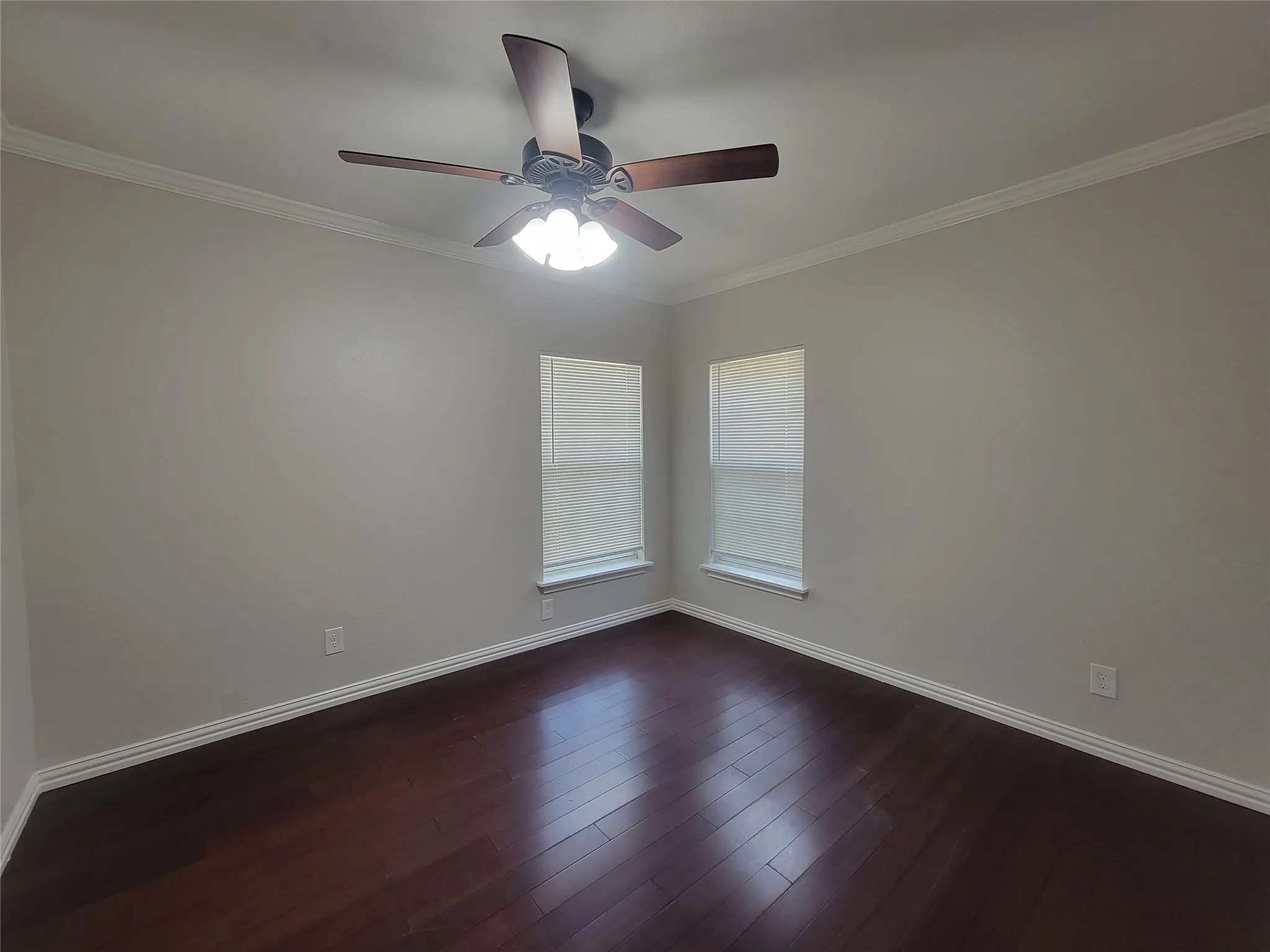 Neutral-toned room featuring rich, wood-finish flooring, white baseboards, and white crown molding