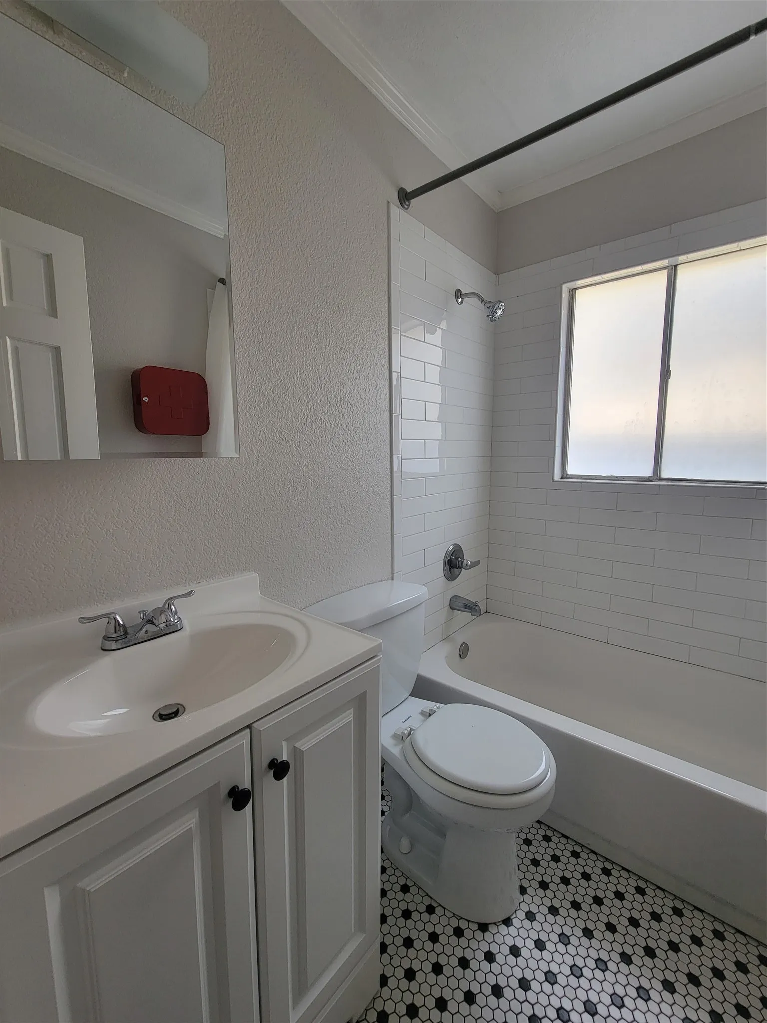 Bathroom featuring black and white hexagonal tile flooring, a white vanity with a single basin sink, a standard toilet, a bathtub with subway tile surround, and a frosted window
