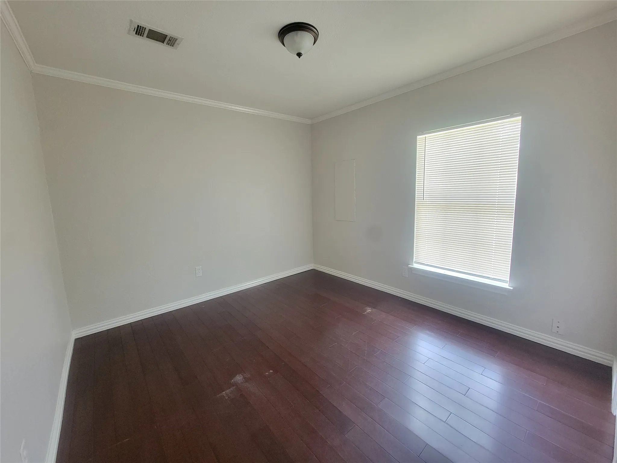 Spacious room featuring wood-finish flooring, light neutral wall paint, white crown molding, and a window with horizontal blinds