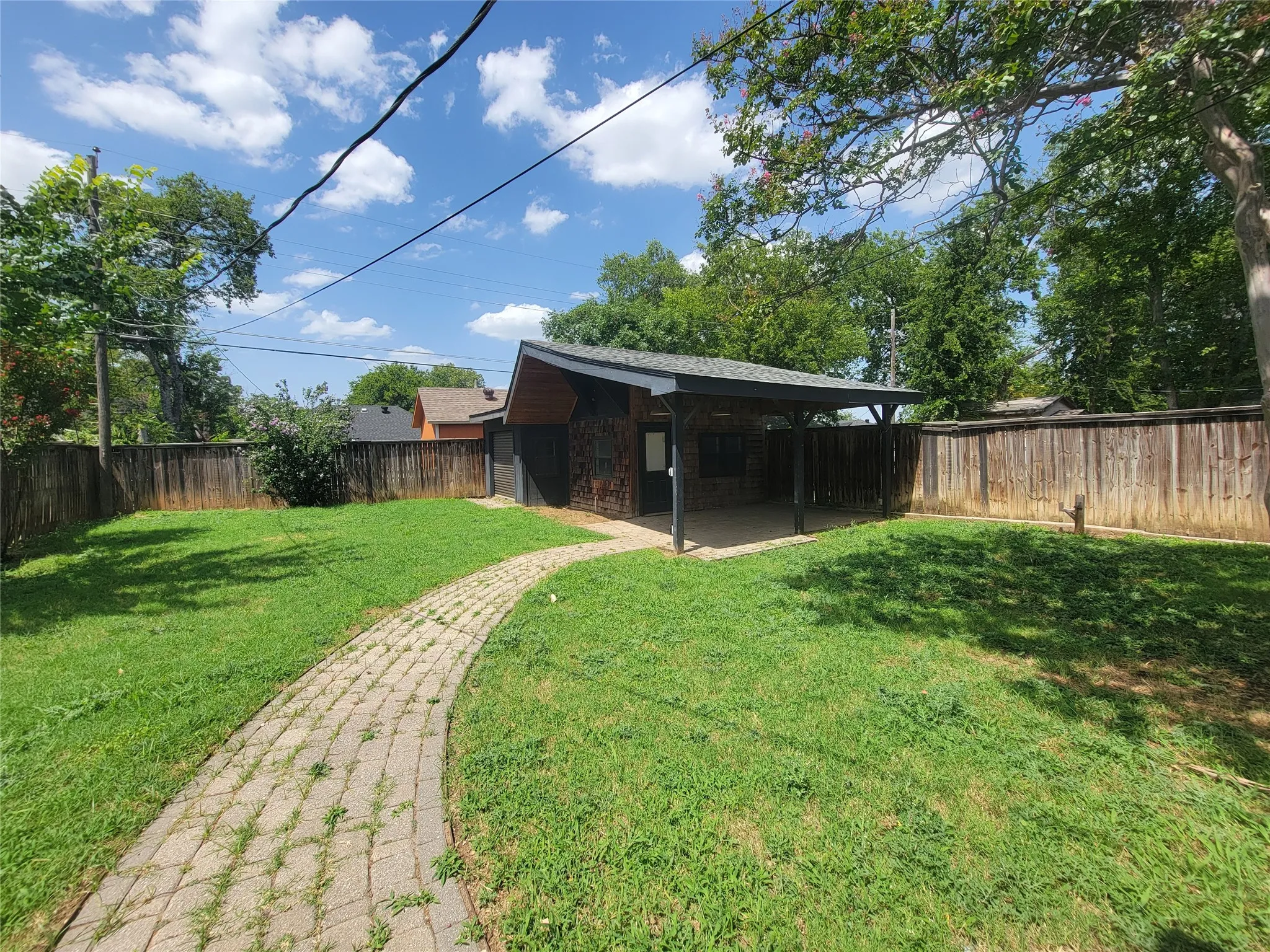Spacious backyard featuring a paver pathway, a detached outbuilding, and a covered patio area with a sloped roof
