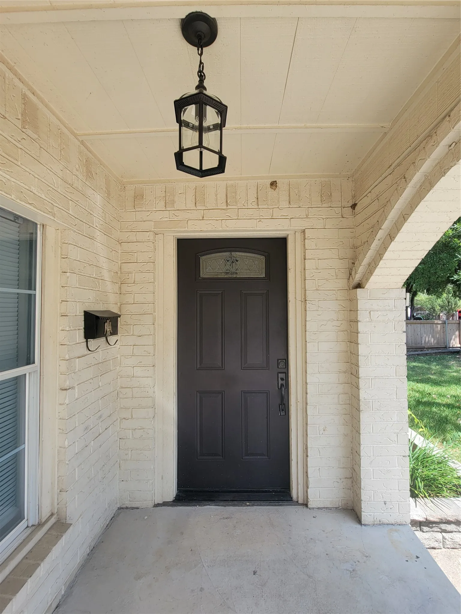 Front entry featuring a dark paneled door with decorative glass insert, a black hanging lantern fixture, and light-colored brick exterior