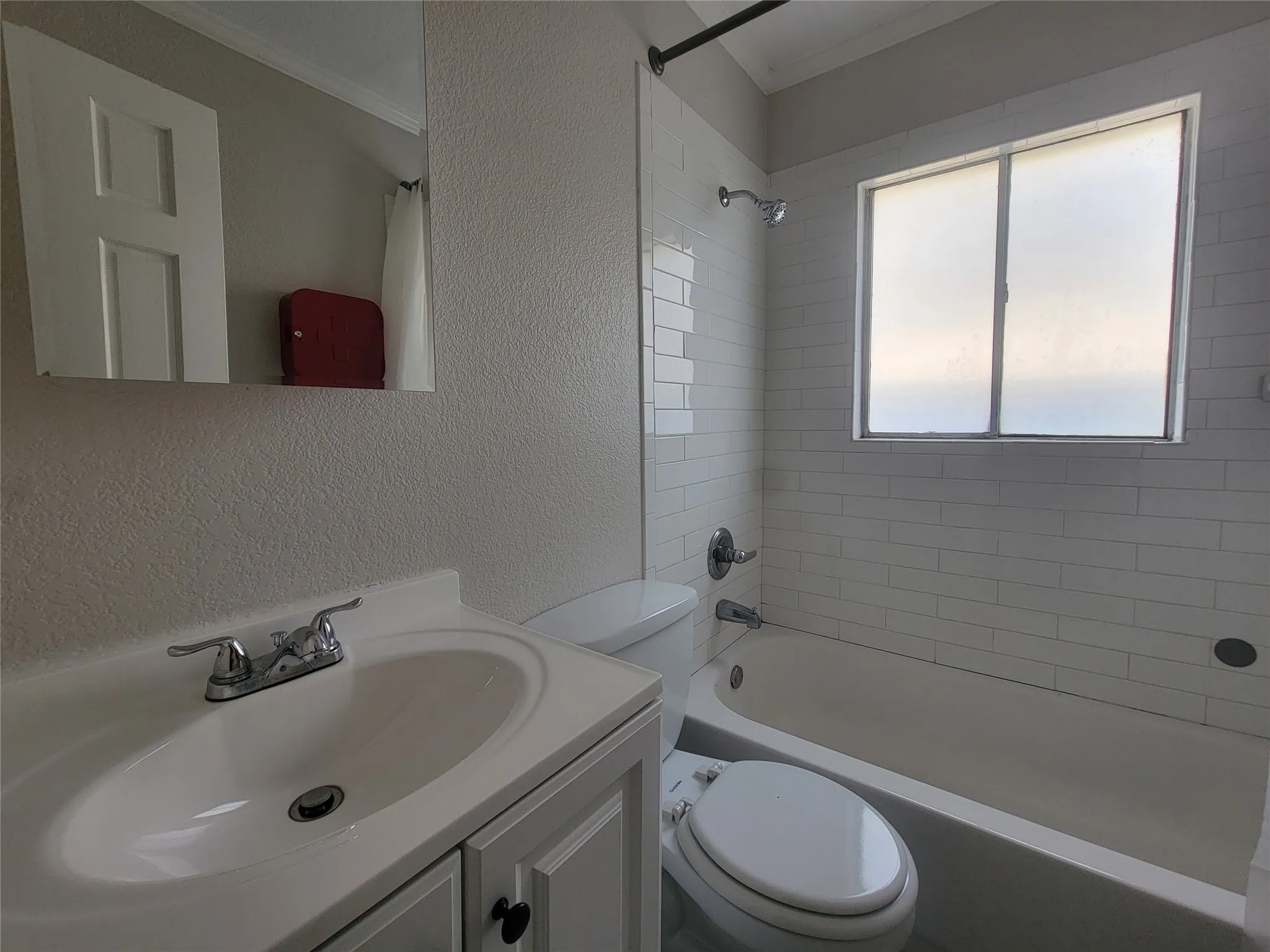 Bathroom featuring a white subway tile surround, a built-in bathtub with shower, a vanity with a white basin sink, and a framed mirror