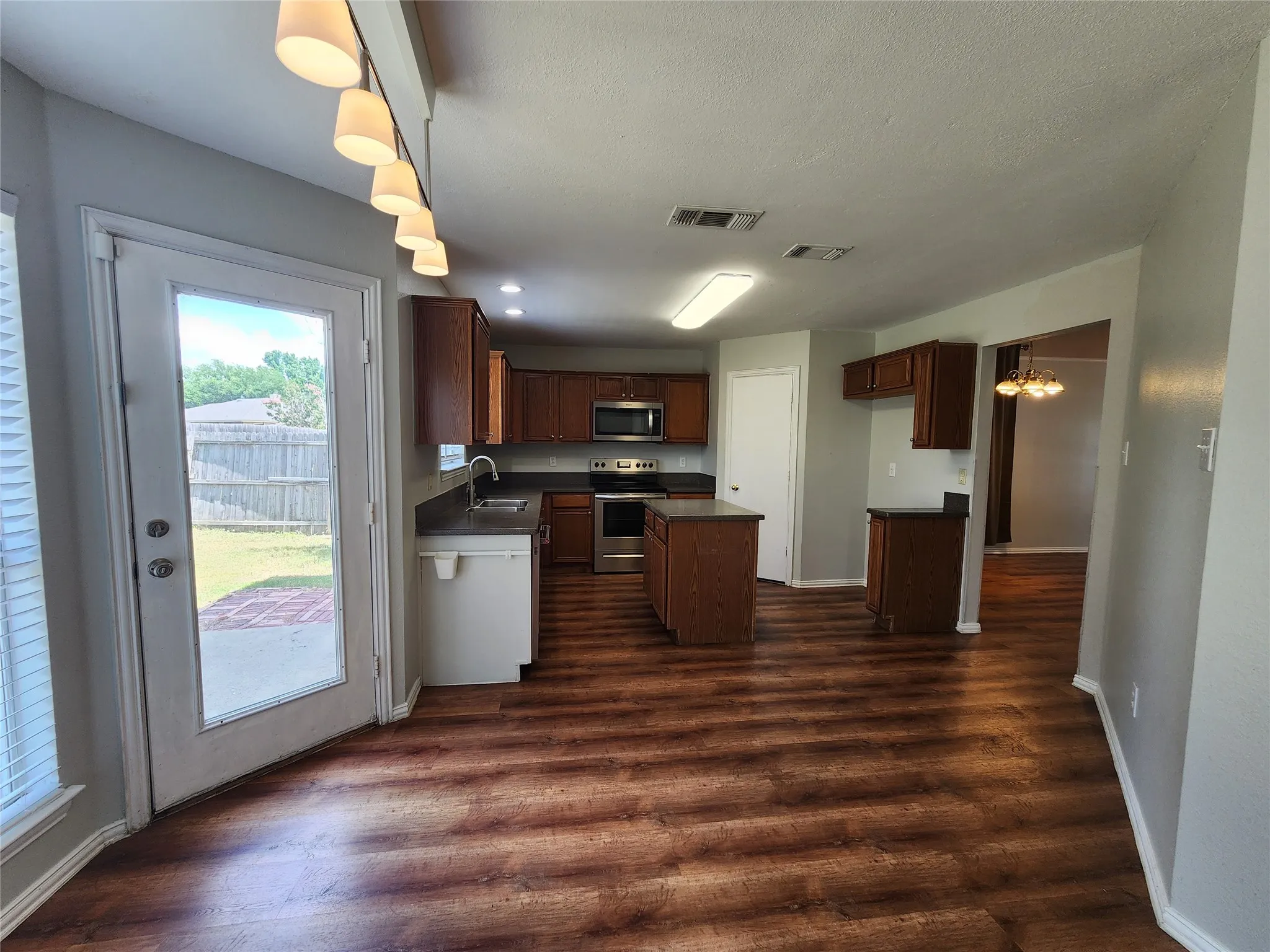 Kitchen featuring rich wood-finish flooring, stainless steel appliances, dark countertops, and a central island