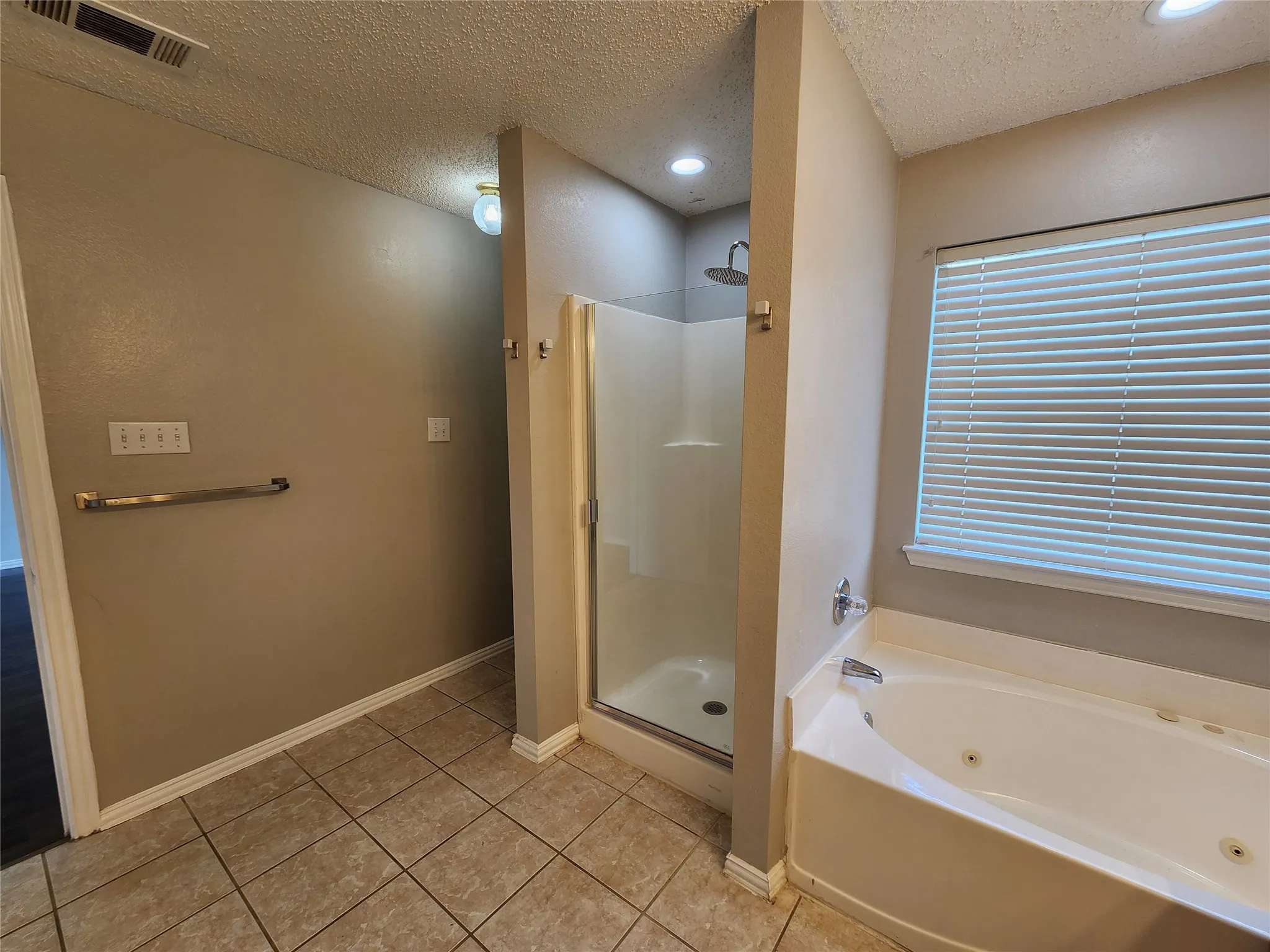 Bathroom featuring a jetted soaking tub, enclosed shower with a rainfall showerhead, and tile flooring