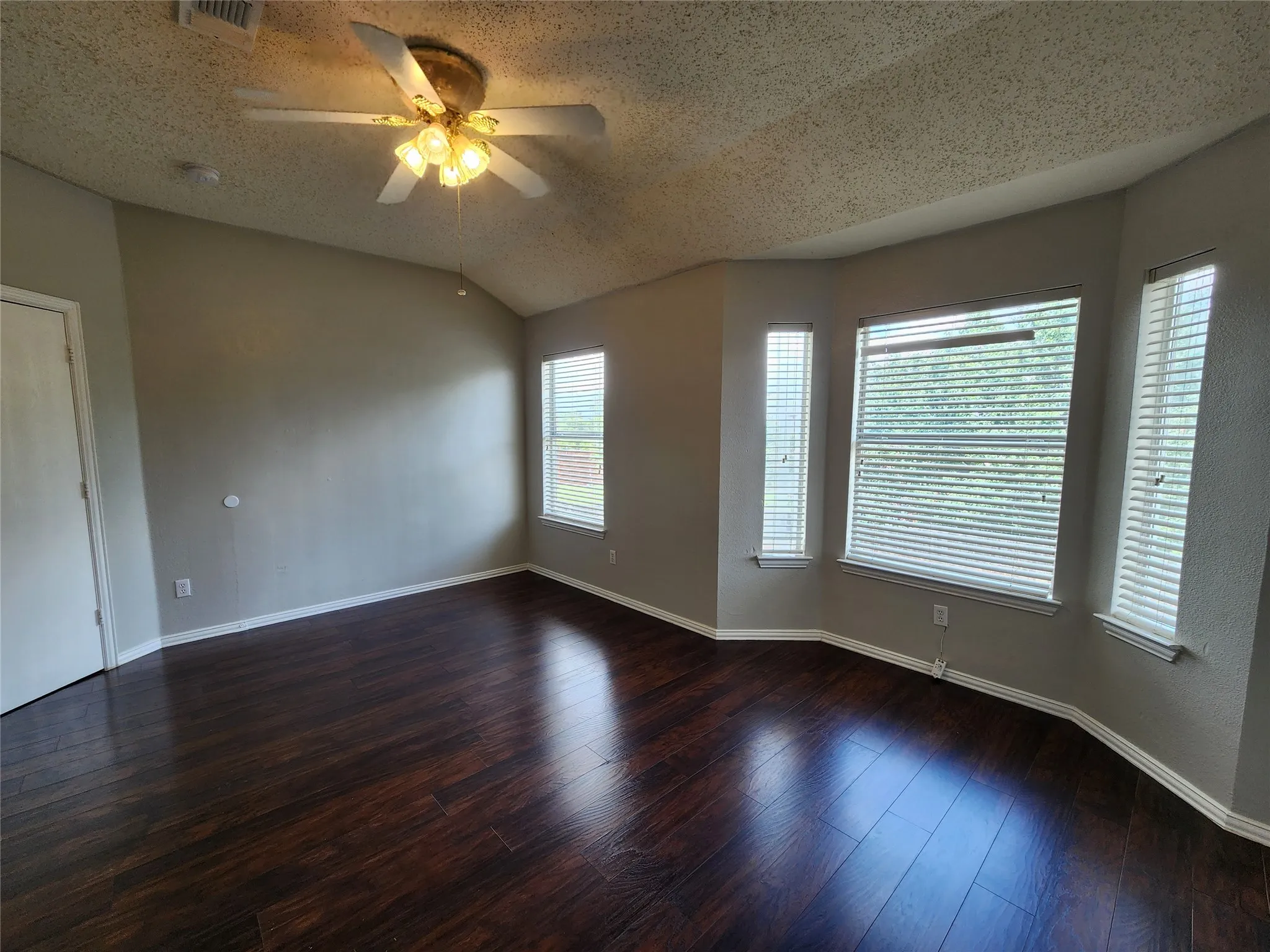 Spacious room featuring dark wood-finish flooring, vaulted ceilings, and a ceiling fan with integrated lighting