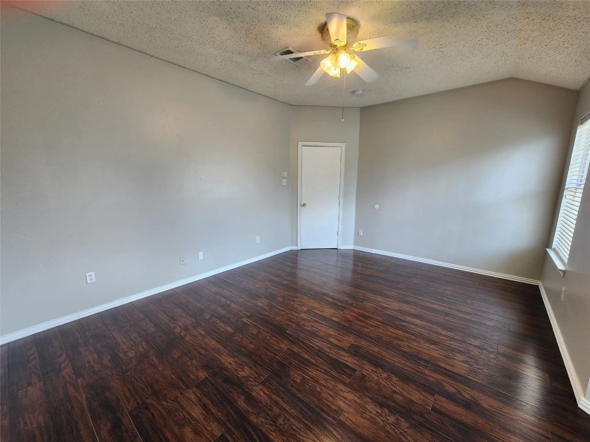 Vaulted ceiling with a ceiling fan, wood-finish flooring, neutral wall paint, white baseboards, and a white interior door