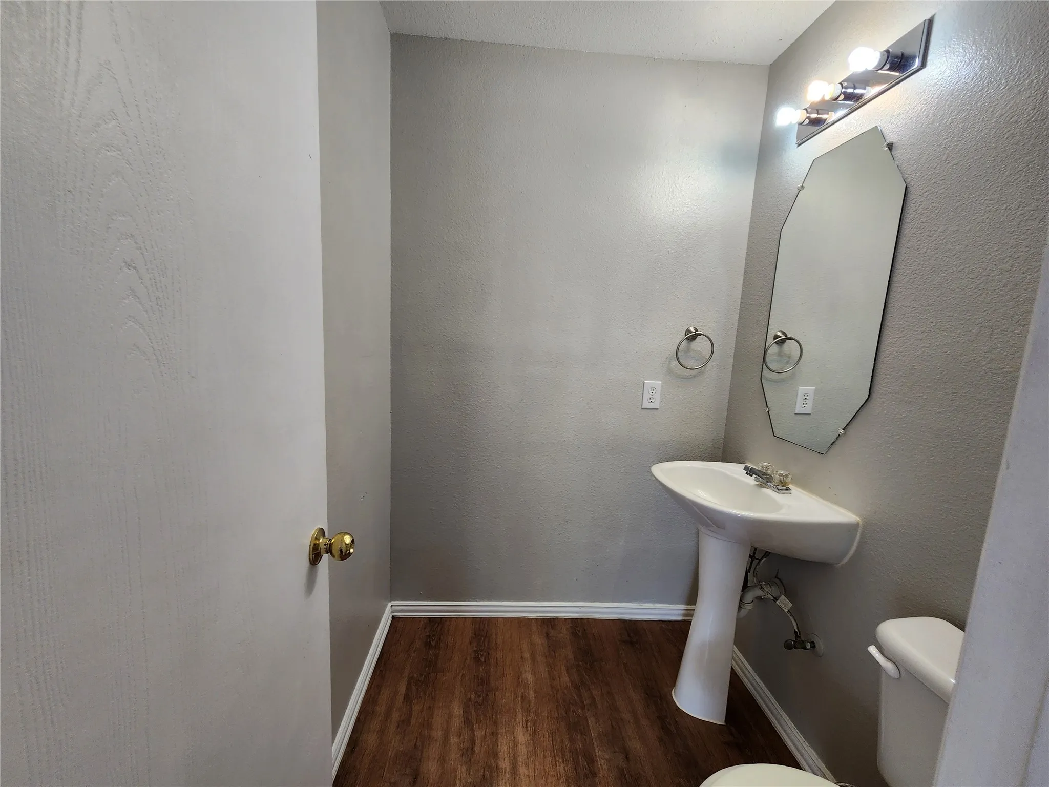 Pedestal sink with chrome fixtures, an octagonal mirror, and a three-light vanity bar
