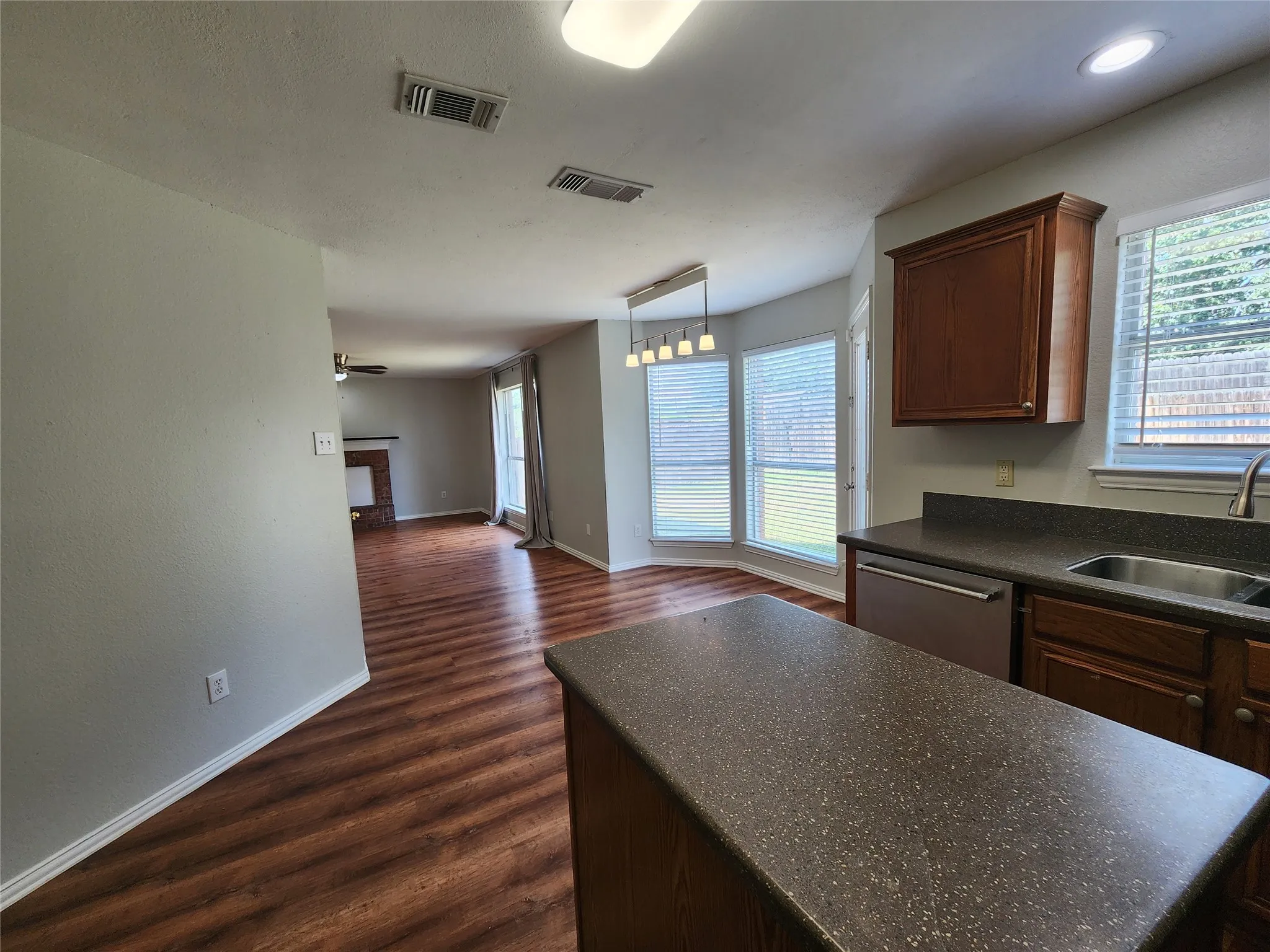 Open-concept kitchen featuring dark wood-finish cabinetry, solid surface countertops, and a stainless steel dishwasher