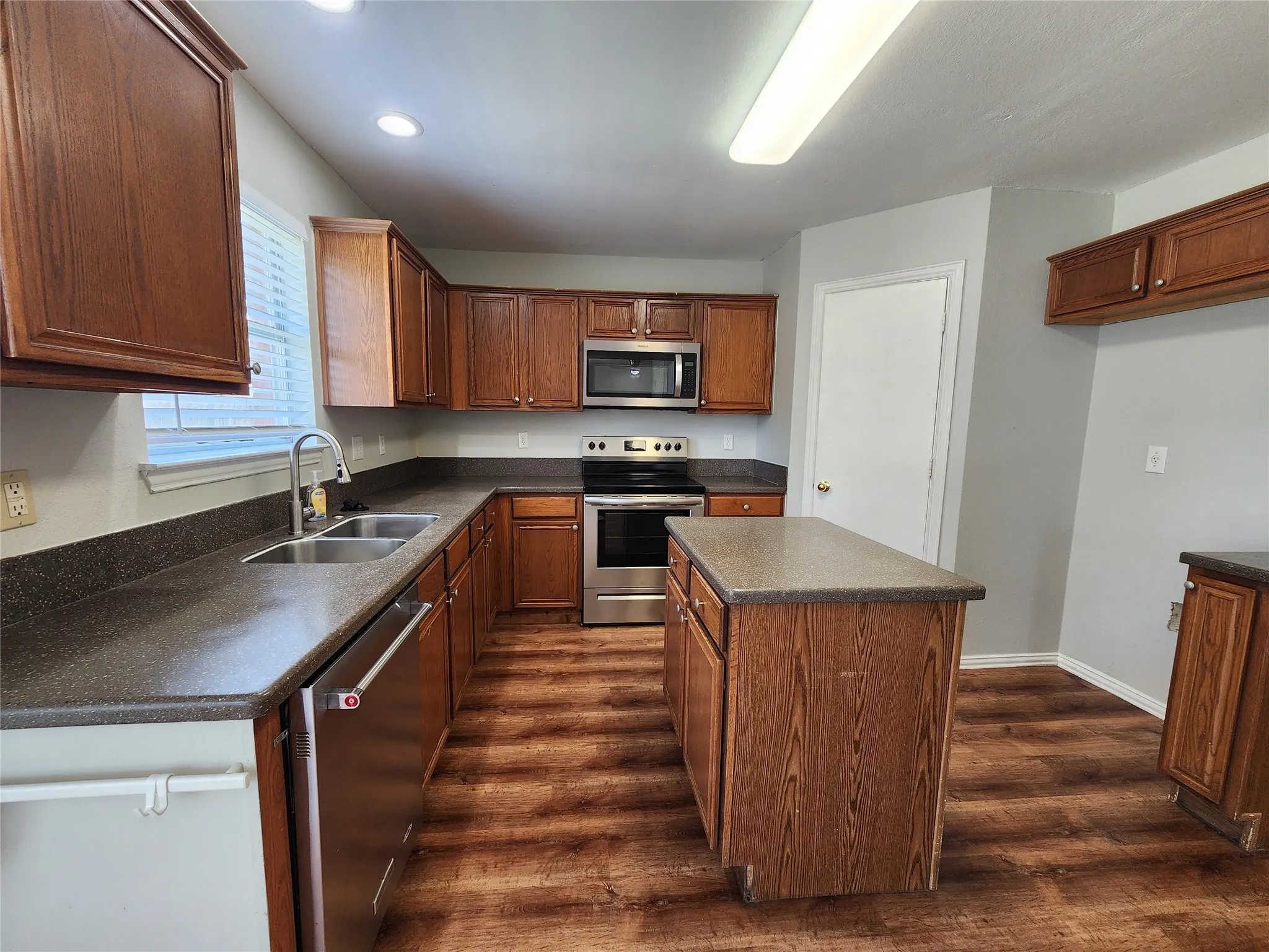 Kitchen featuring wood-finish flooring, dark countertops, wood cabinetry, stainless steel appliances, and a central island
