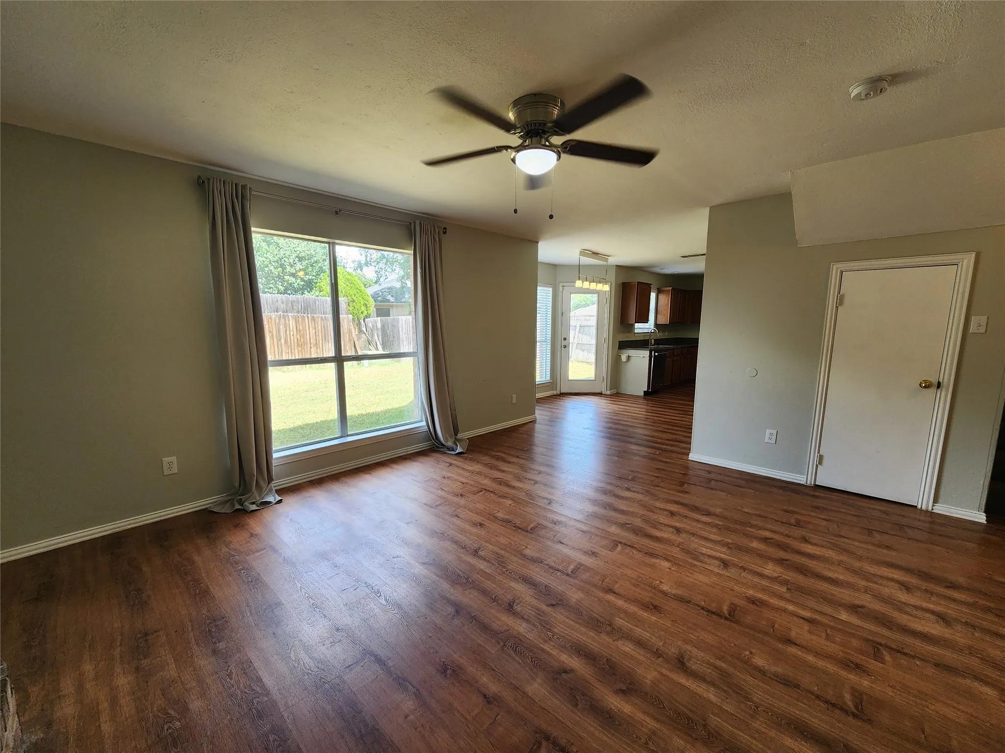 Living area featuring wood-finish flooring, a large window, and a ceiling fan