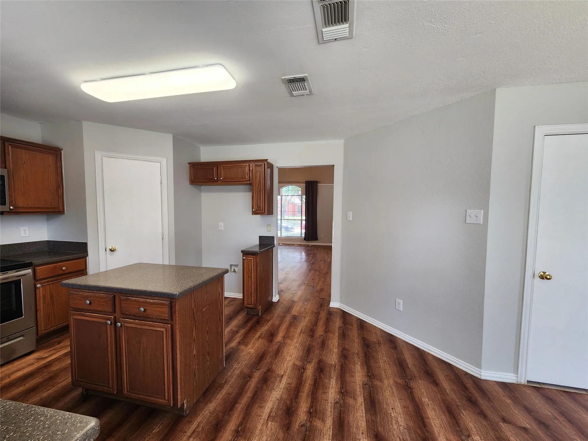 Kitchen featuring wood-finish flooring, a central island with storage, dark countertops, and wood cabinetry