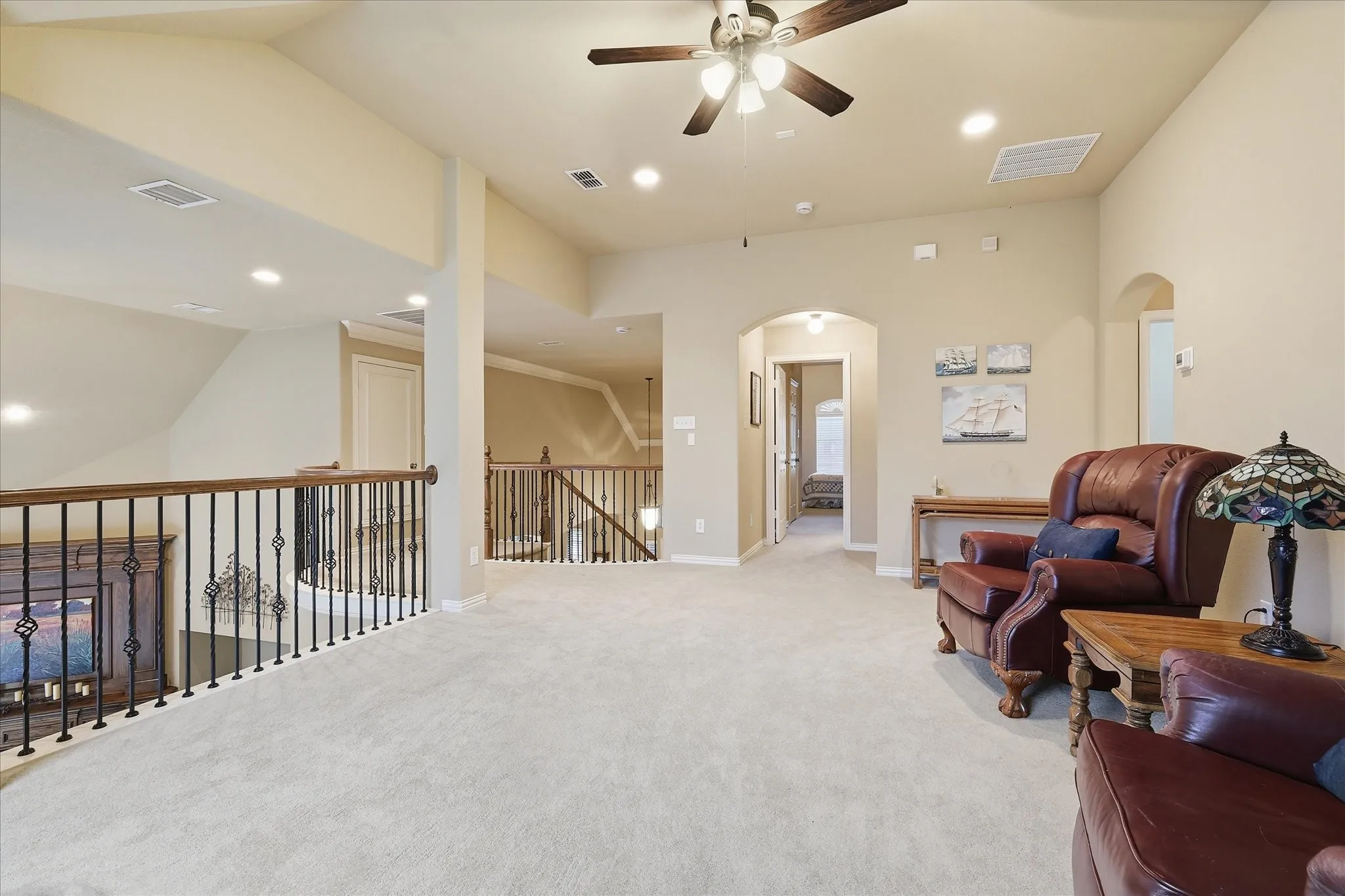Spacious loft area featuring light-colored carpeting, recessed lighting, arched doorways, a ceiling fan, and wrought iron balusters with wood handrails