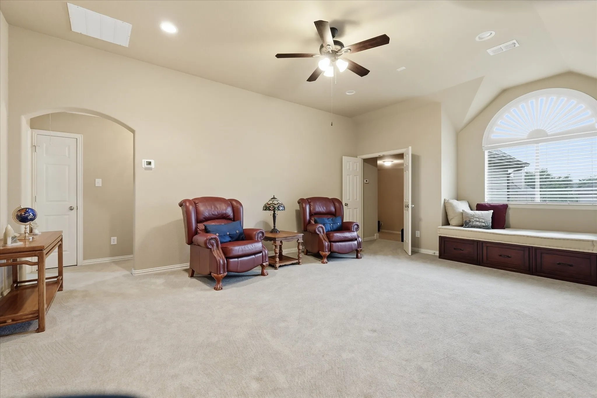 Spacious secondary living area featuring a large arched window with a built-in window seat and storage, vaulted ceiling, recessed lighting, and a ceiling fan