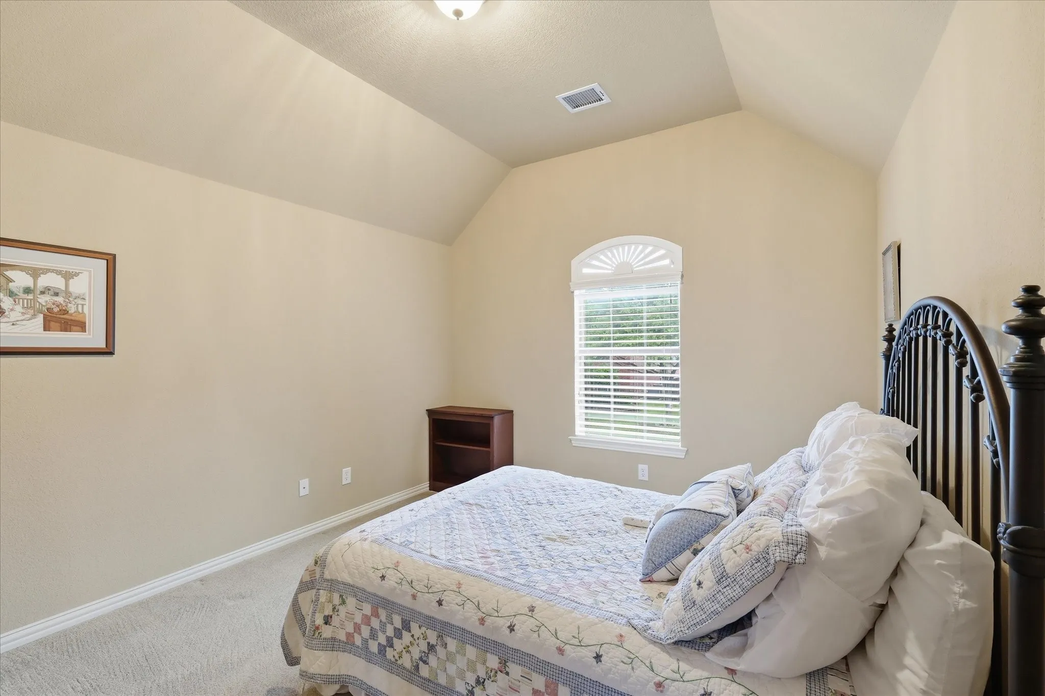 Vaulted ceiling room featuring a decorative arched window with blinds, neutral wall paint, and light-colored carpeting