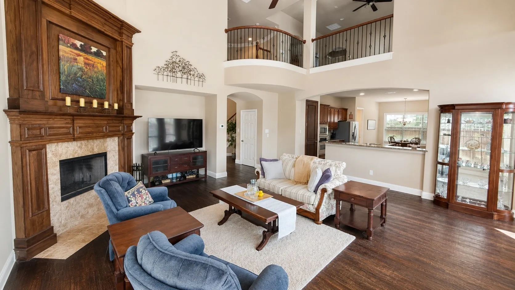 Spacious living area featuring high ceilings, dark wood-finish flooring, and a stone fireplace with an ornate wood mantel